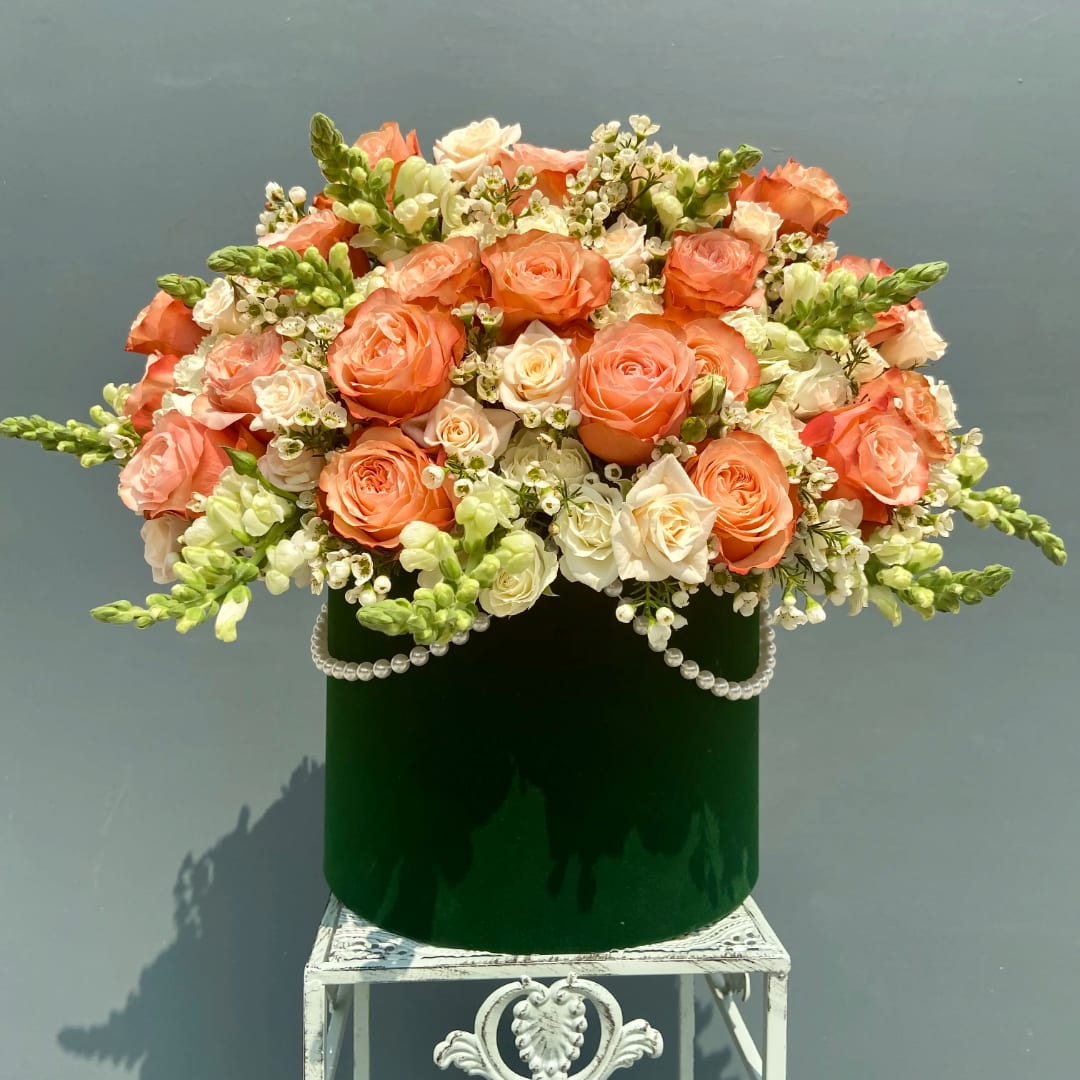 Peach and white roses arranged in a green velvet box with pearl trim