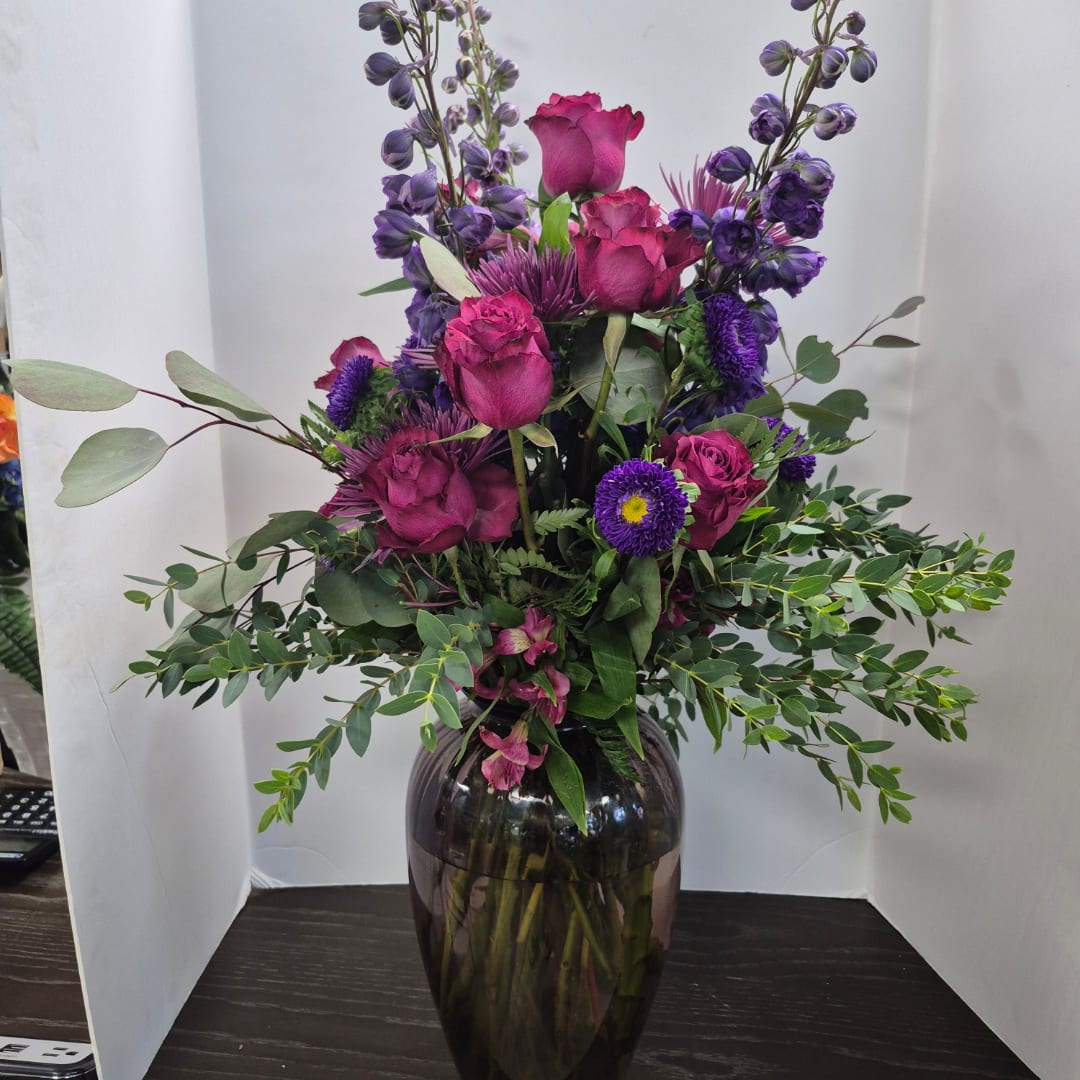 Purple and pink floral arrangement in a dark glass vase