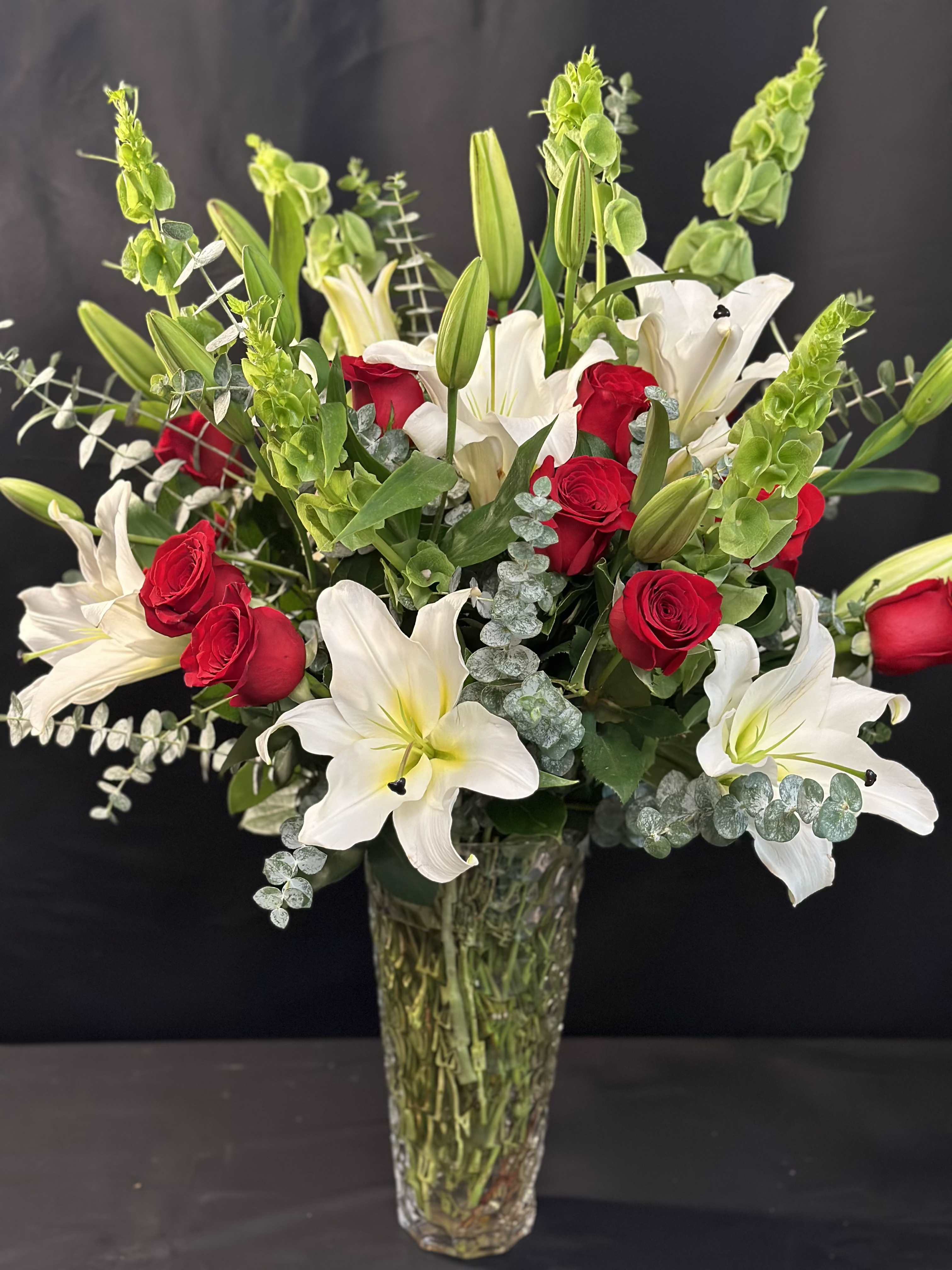 Red roses and white lilies in a clear glass vase with greenery
