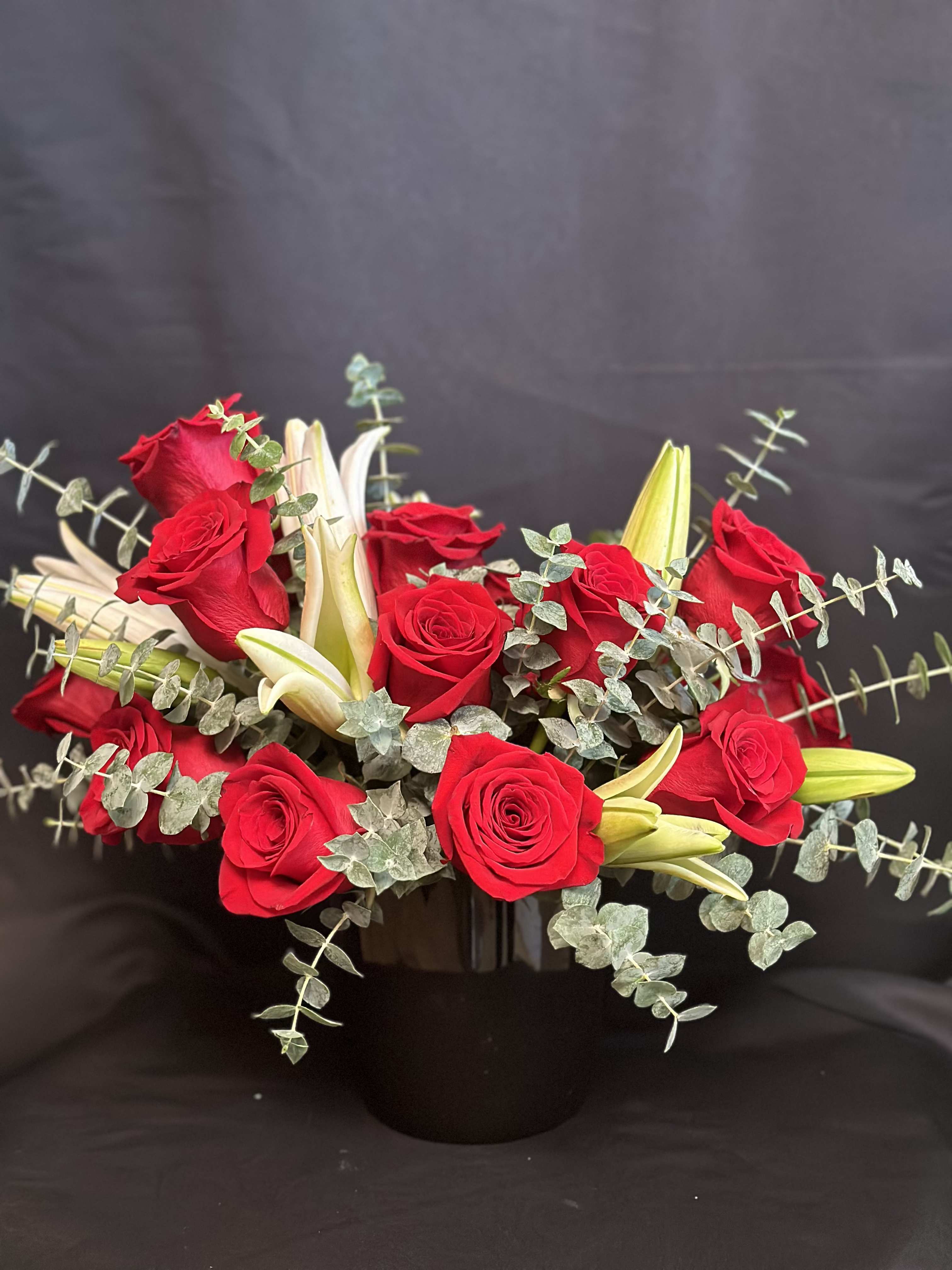 Red roses and white lilies in a black vase with trailing eucalyptus