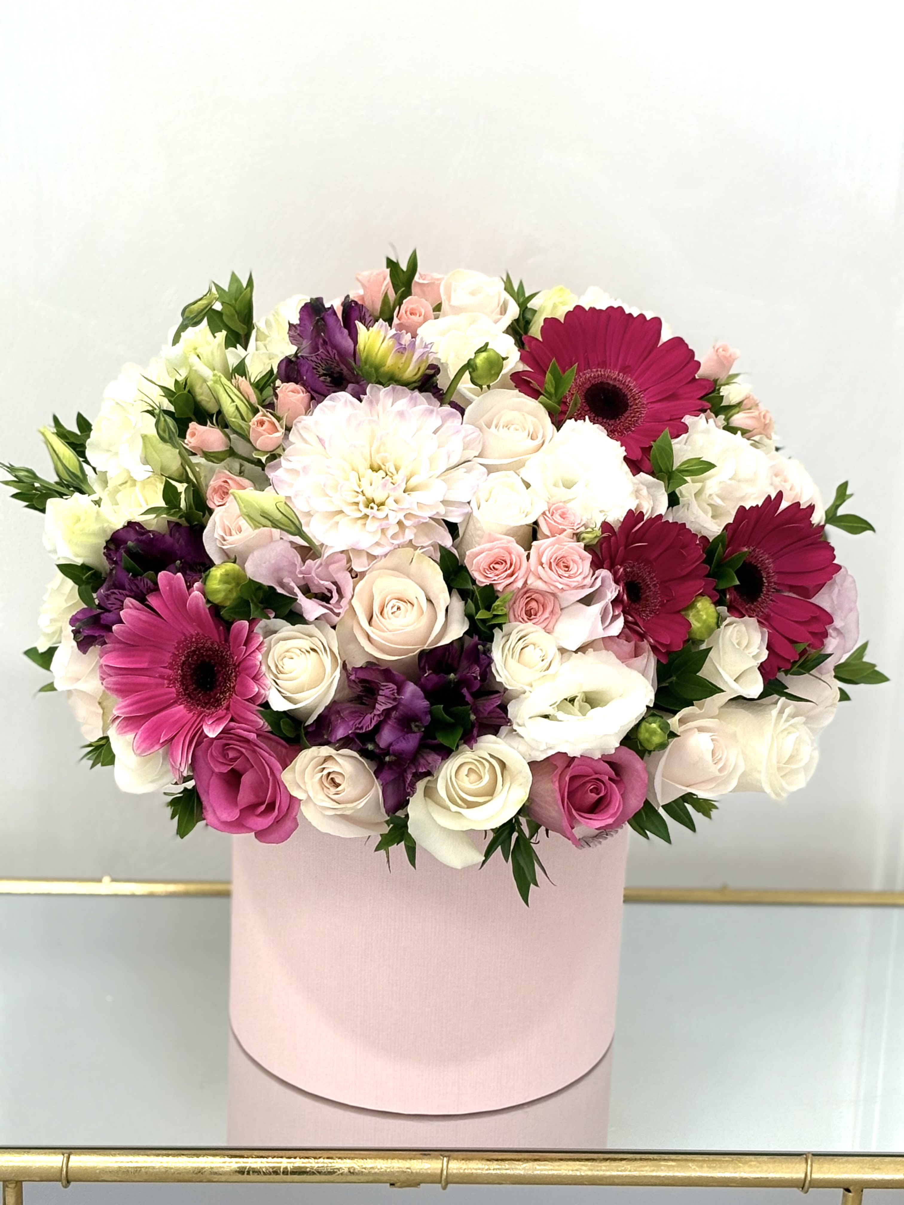 Round bouquet of pink, white, and purple flowers in a pink box