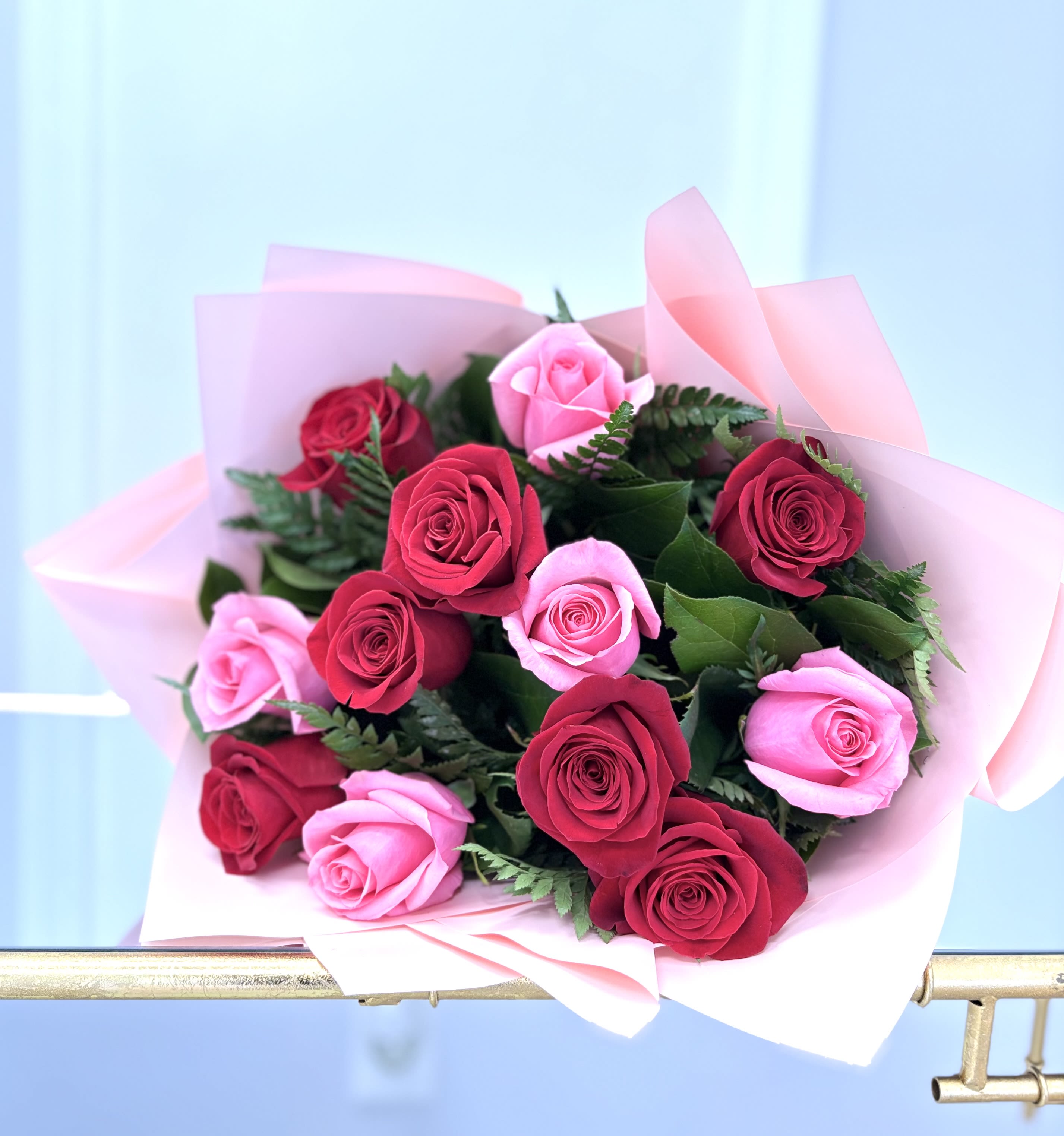 Hand-tied bouquet of red and pink roses wrapped in soft pink paper