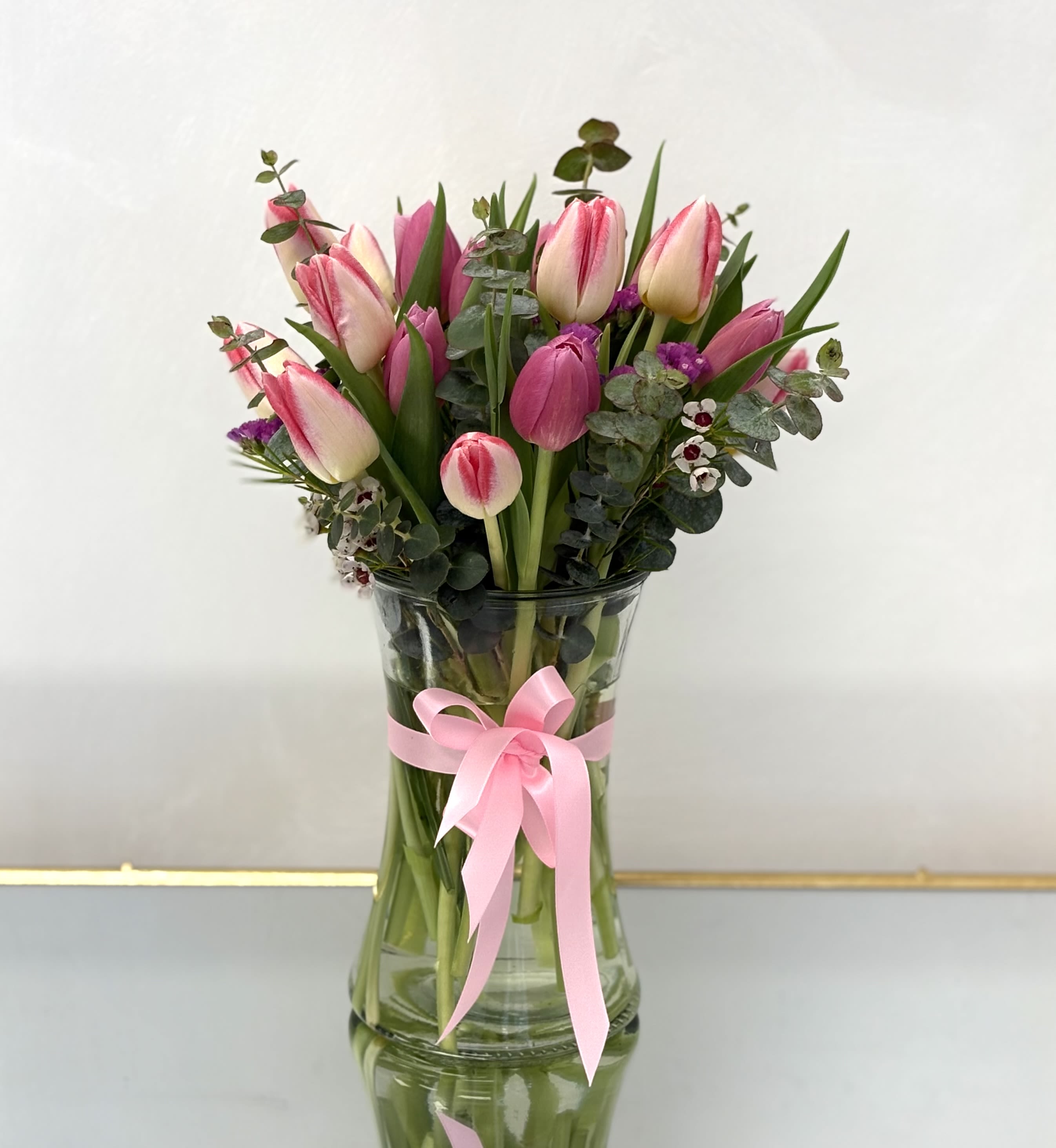 Pink tulips in a clear glass vase with a pink ribbon