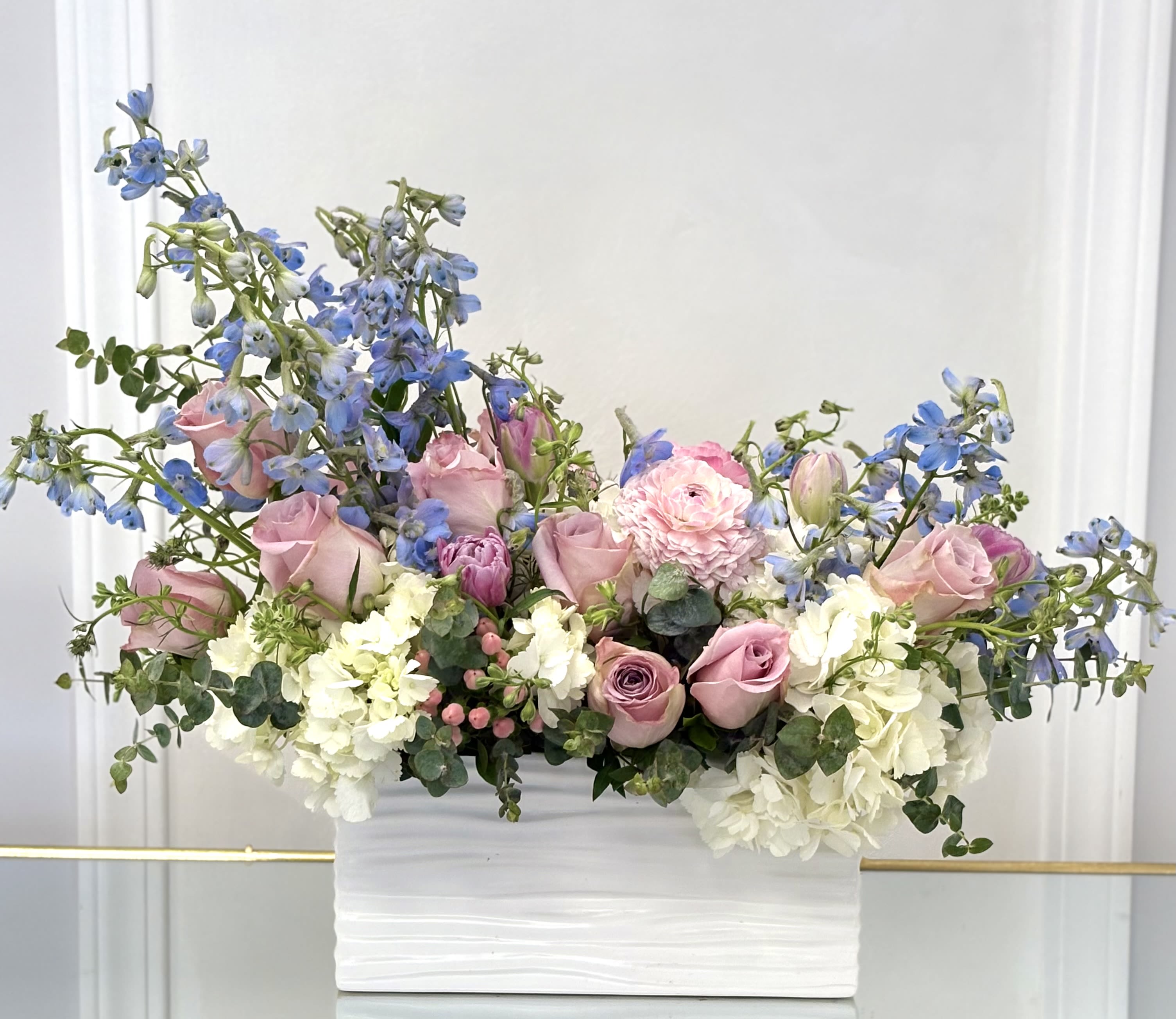 Pink roses and blue delphinium in a white rectangular vase
