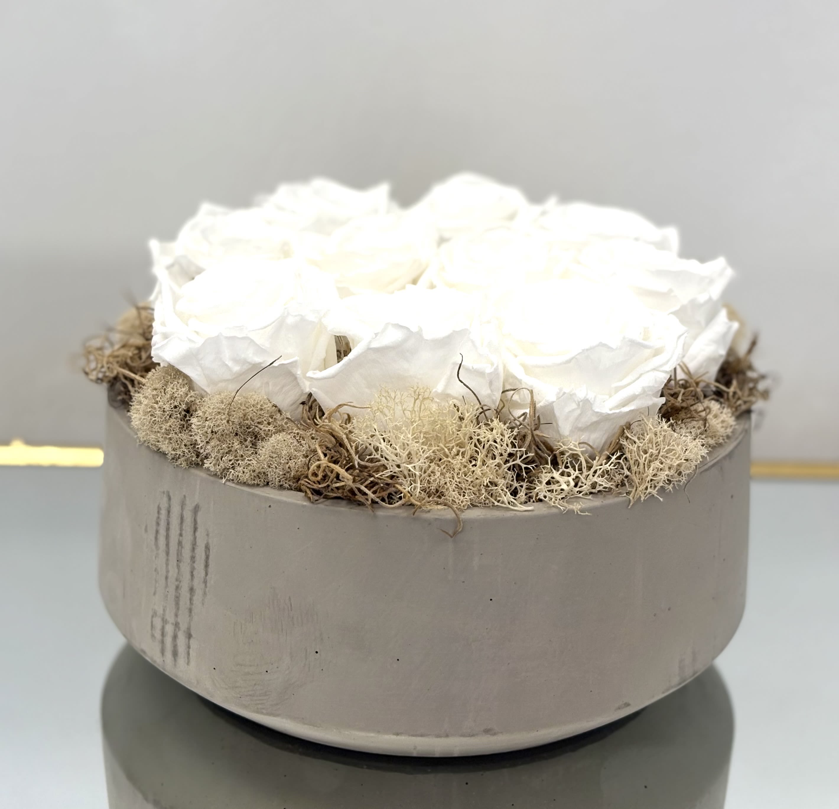 White roses arranged in a round gray box with dried moss