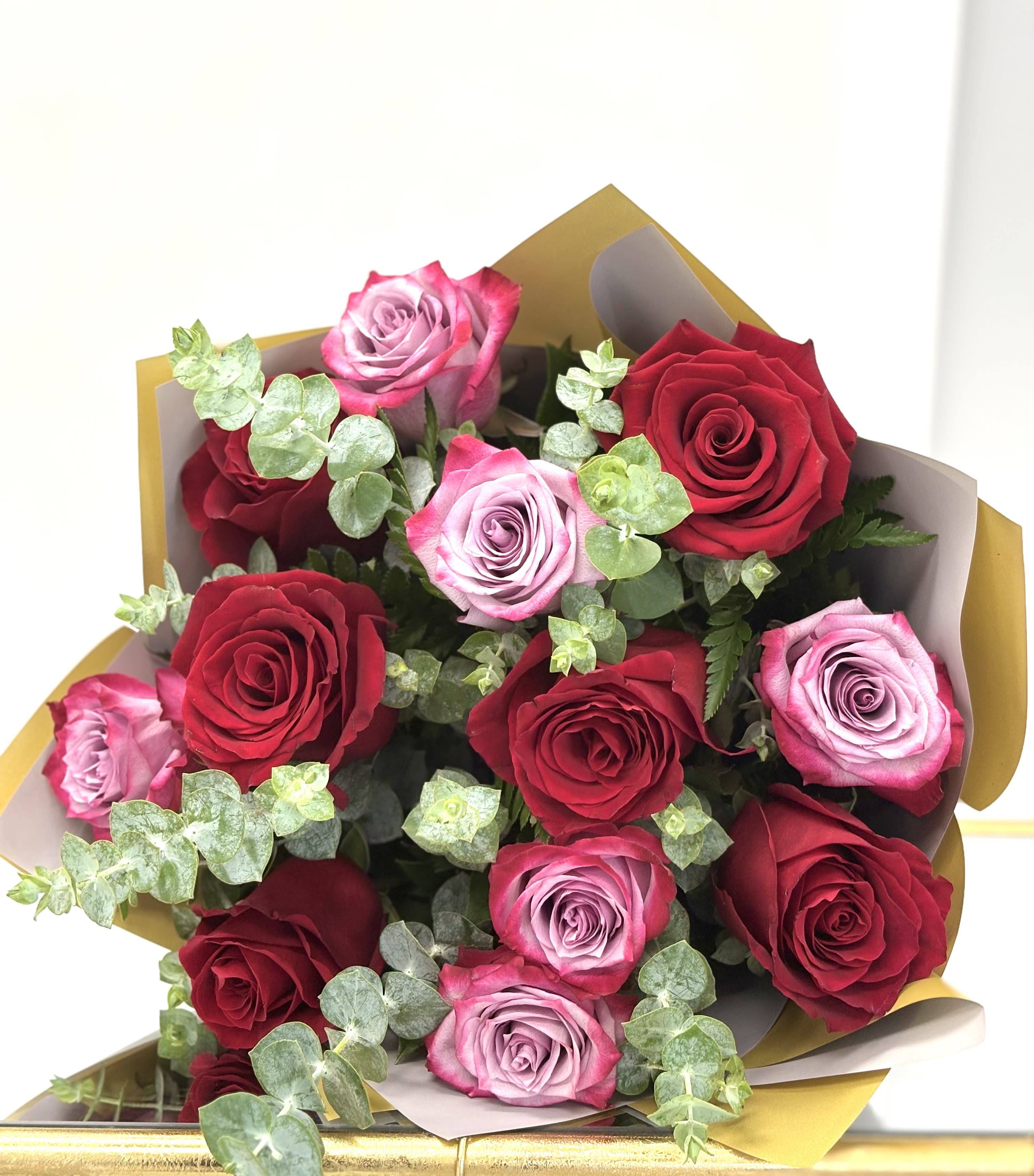 Bouquet of red and lavender roses wrapped in gold and white paper