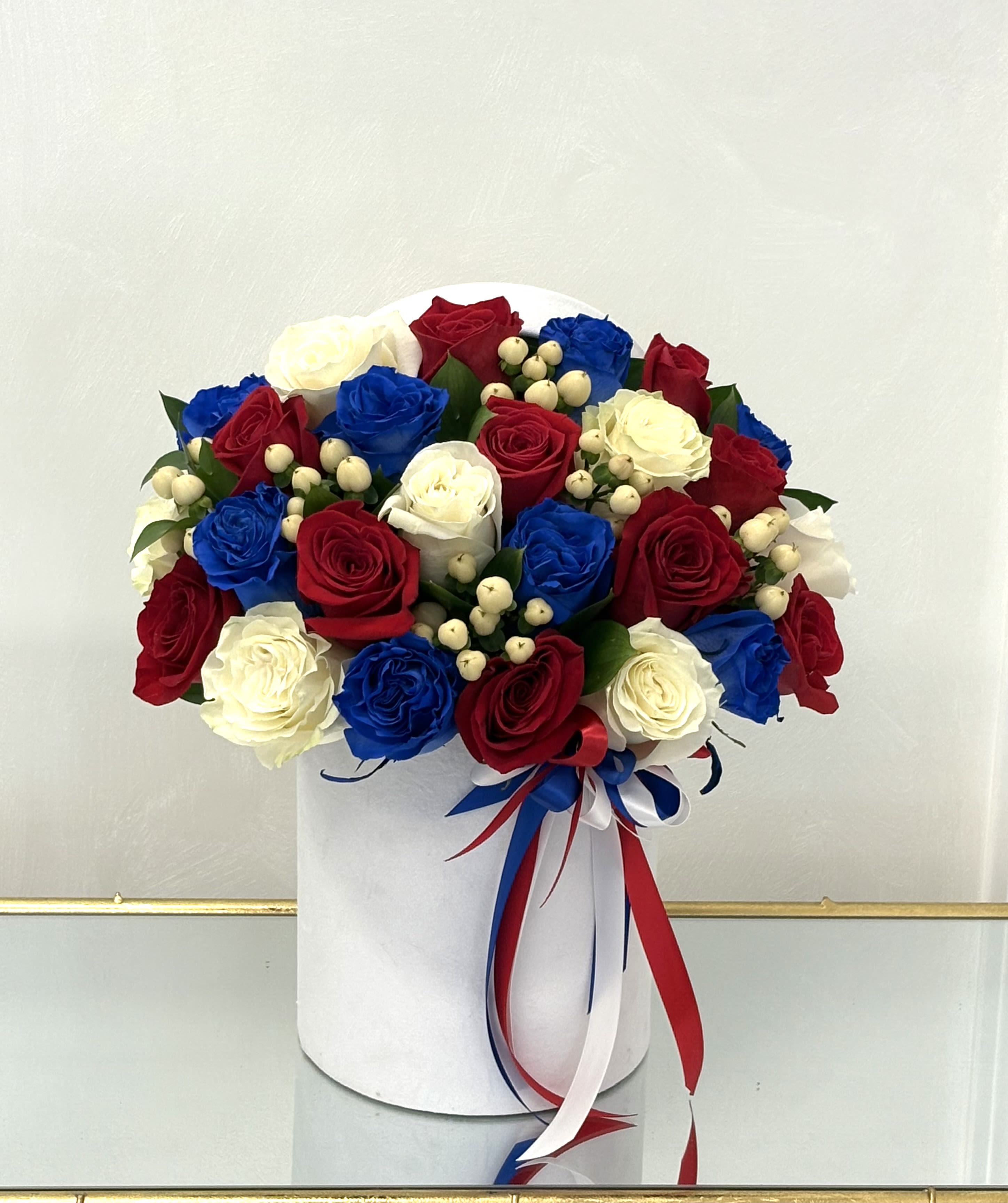 Red, white, and blue roses arranged in a white hat box with ribbon