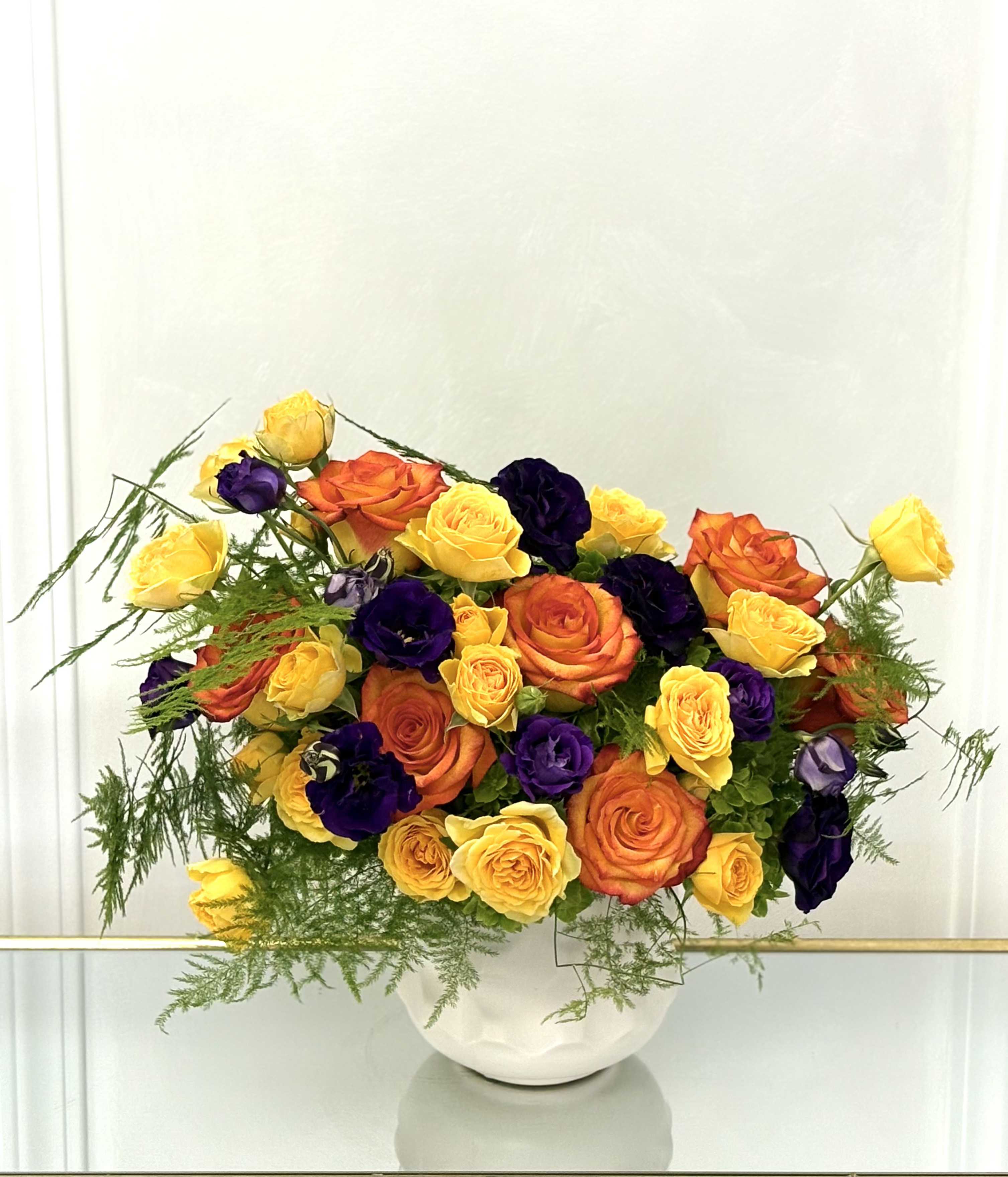 Bouquet of yellow, orange, and purple roses in a white vase