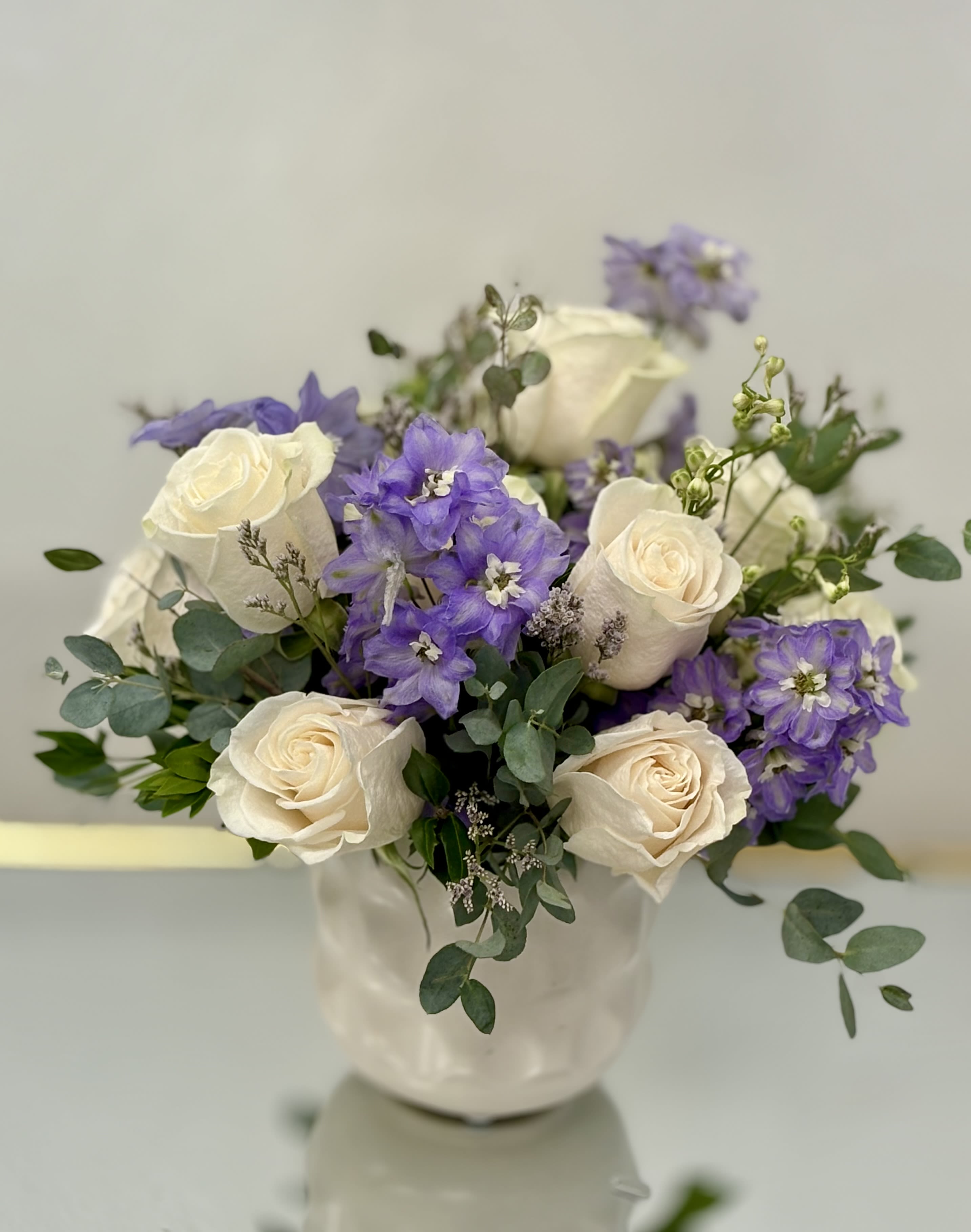 White roses and purple flowers arranged in a white vase