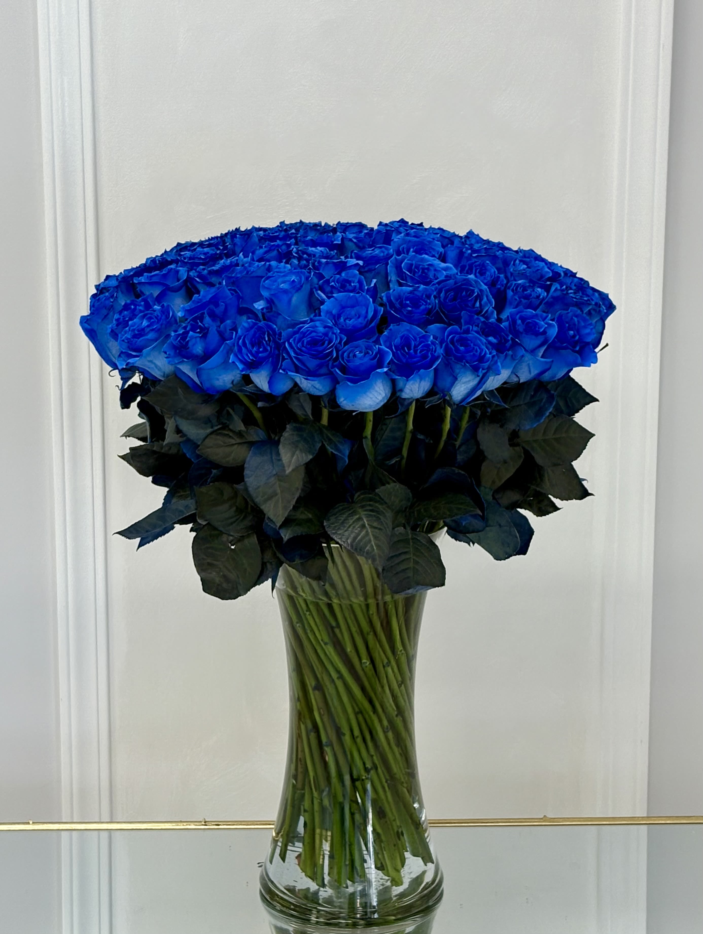 Large bouquet of vivid blue roses in a clear glass vase