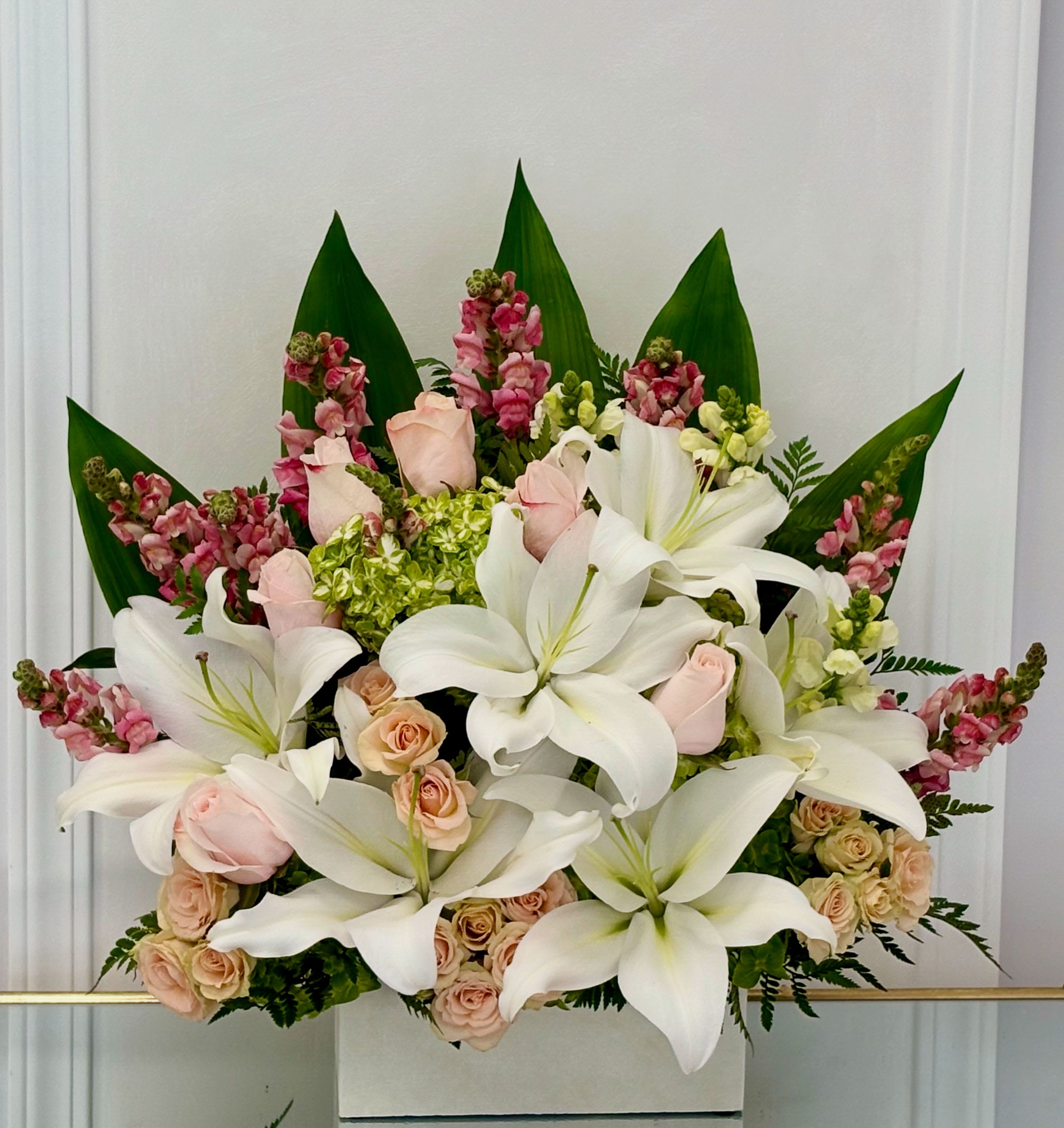 White lilies and pale roses arranged in a box with pink accents