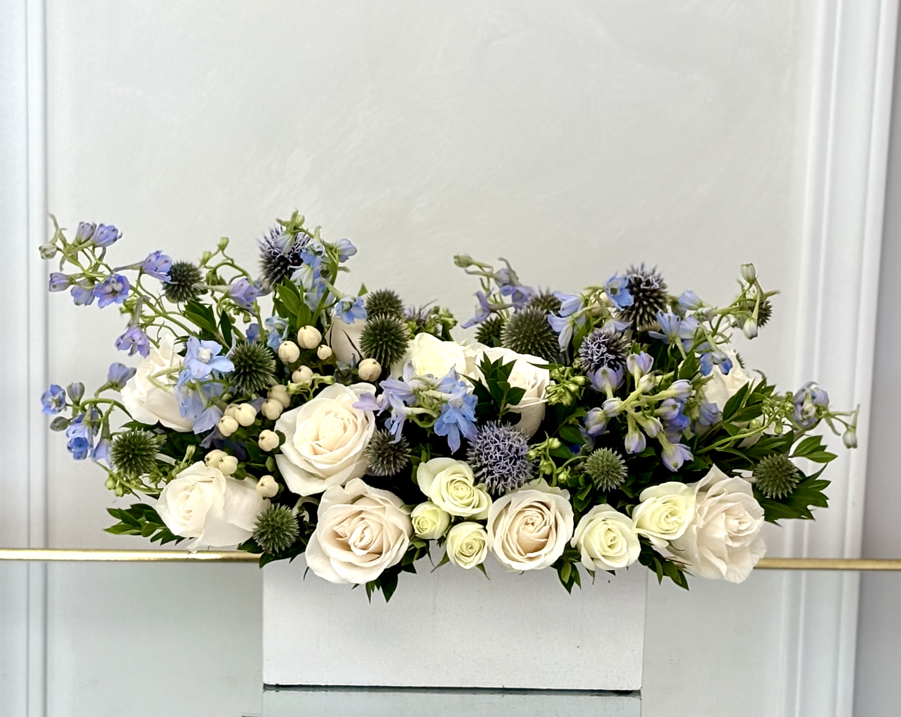White roses and blue flowers arranged in a white box