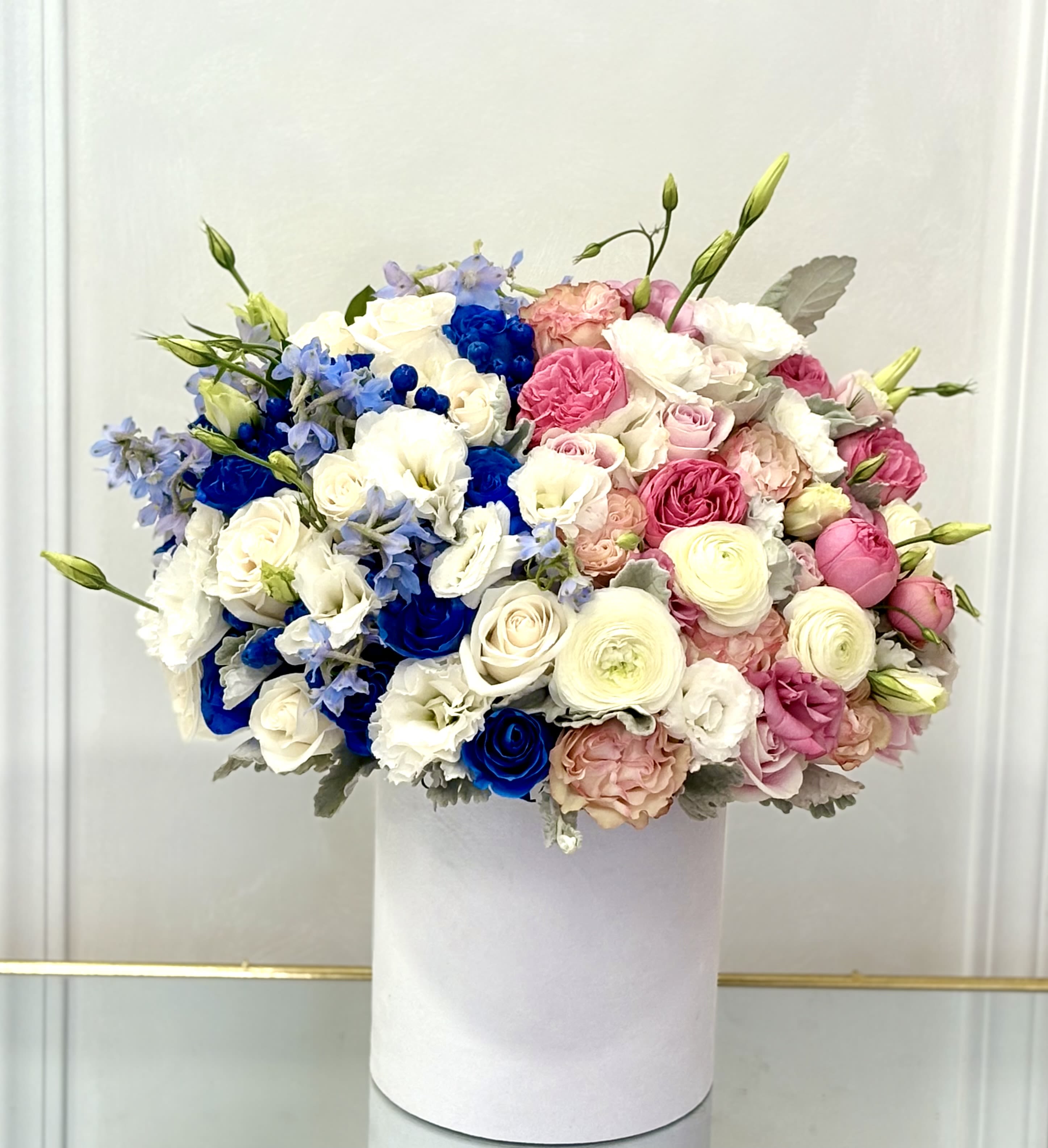 Round bouquet of pink, white, and blue flowers in a white box