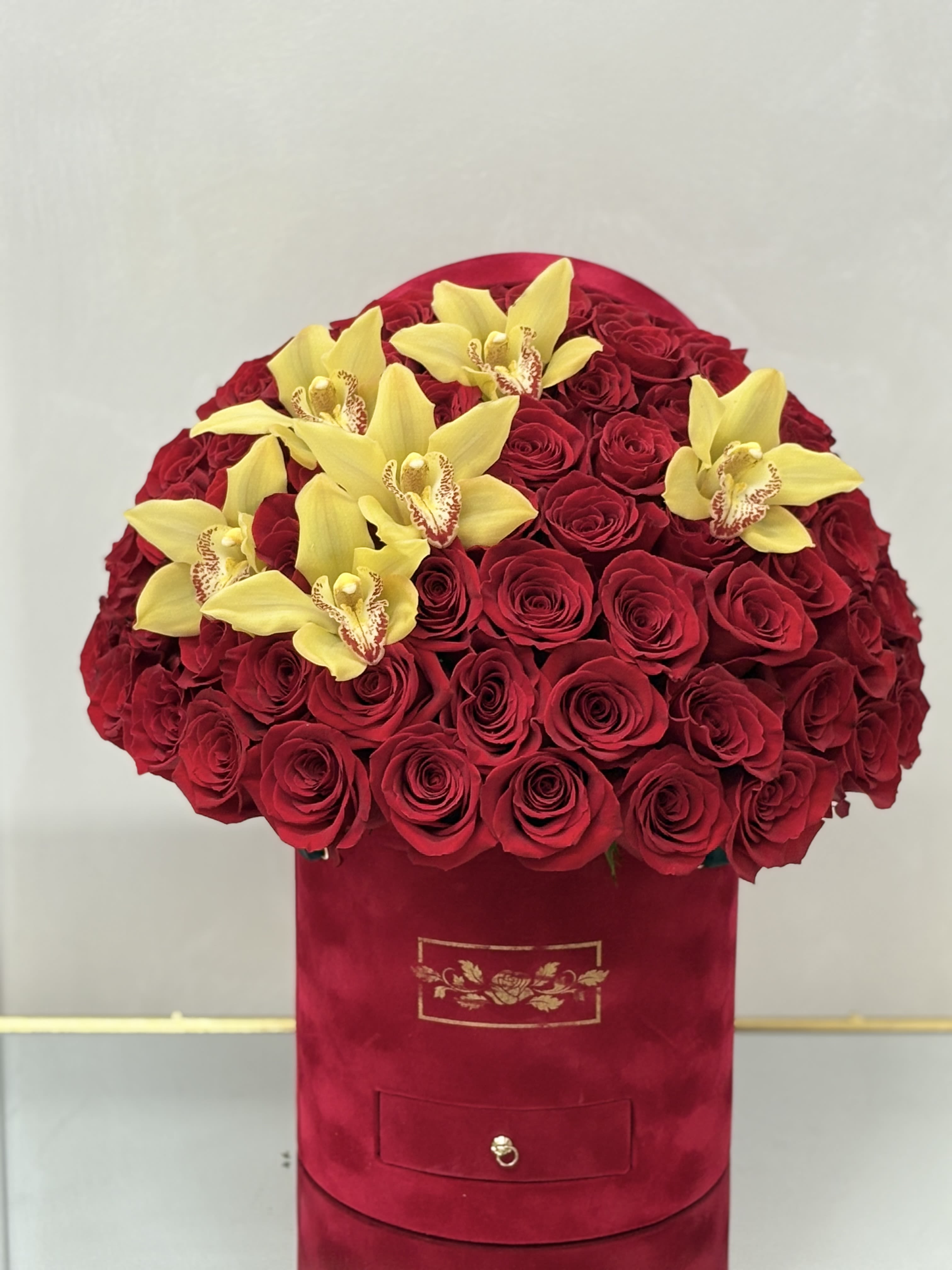 Round red hat box filled with red roses and topped with yellow orchids