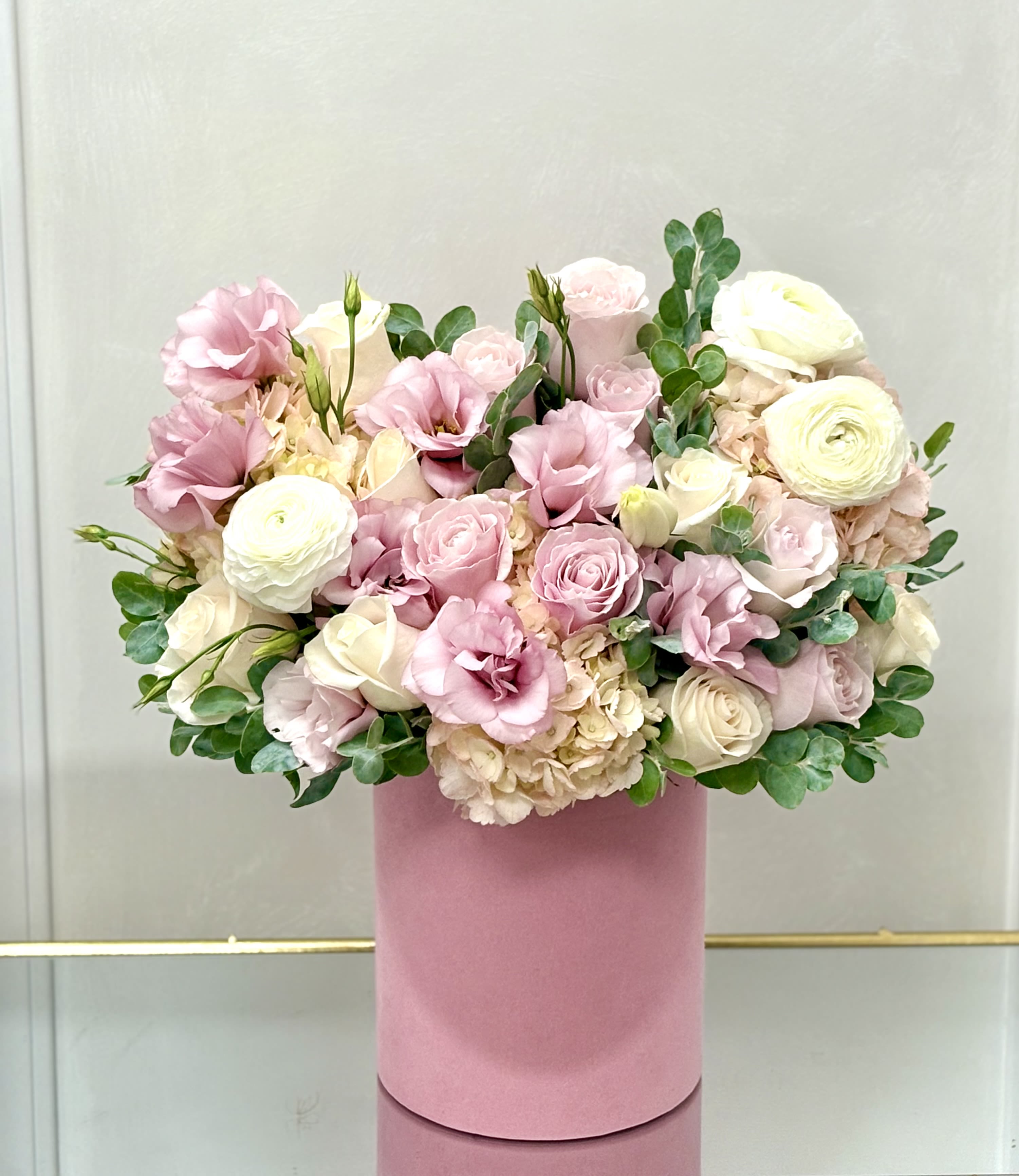 Pink and white roses with ranunculus in a pink hat box