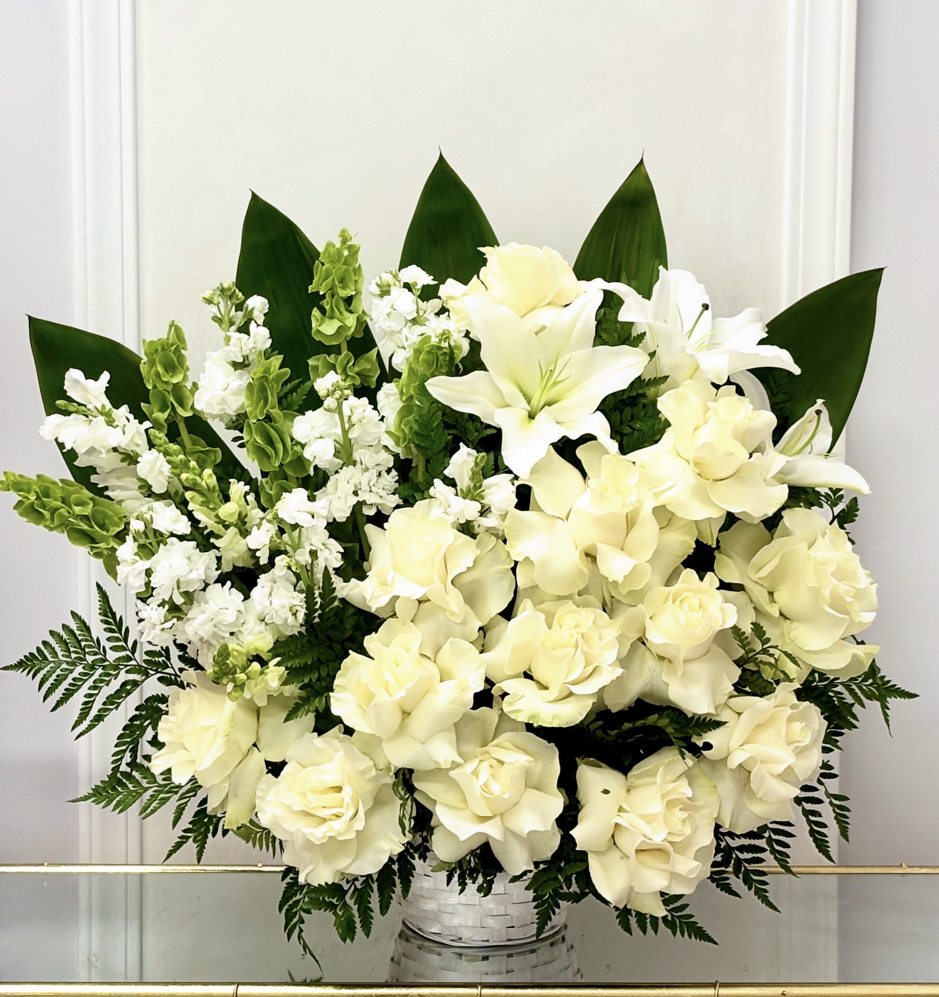 White floral arrangement in a woven basket with dark green leaves