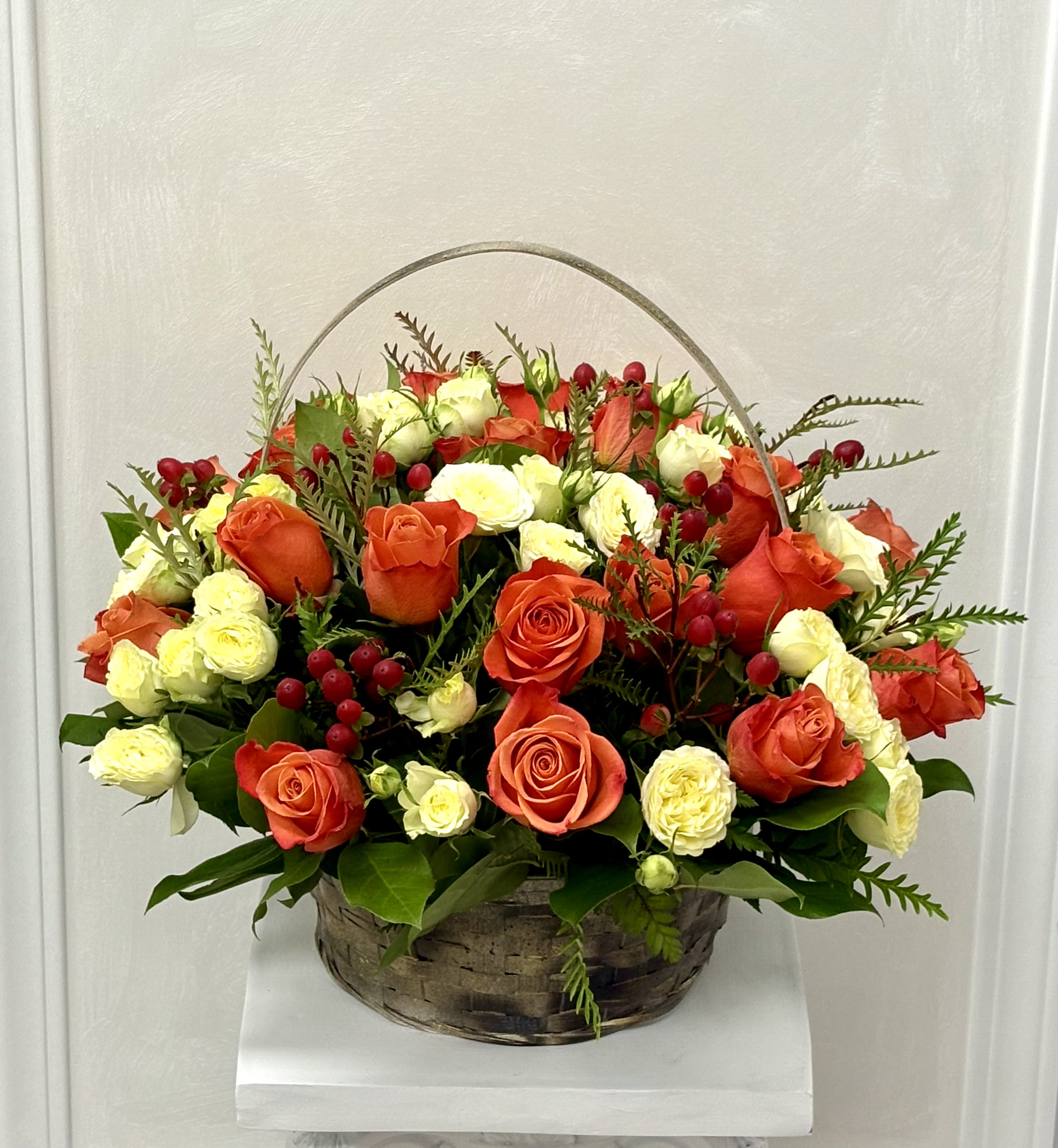 Basket arrangement of orange and white roses with red berries