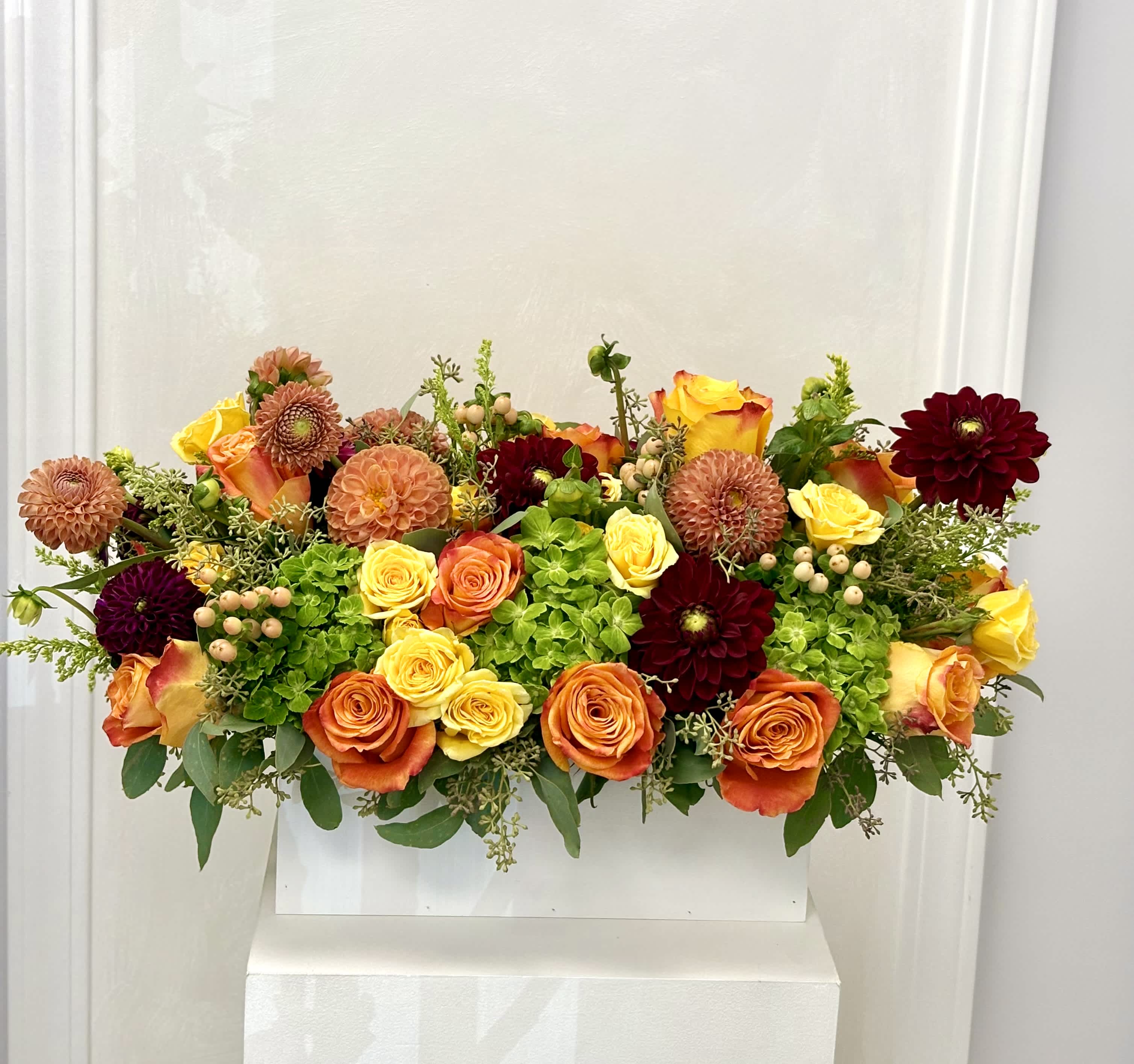 Mixed bouquet of orange, yellow, and burgundy flowers in a white container