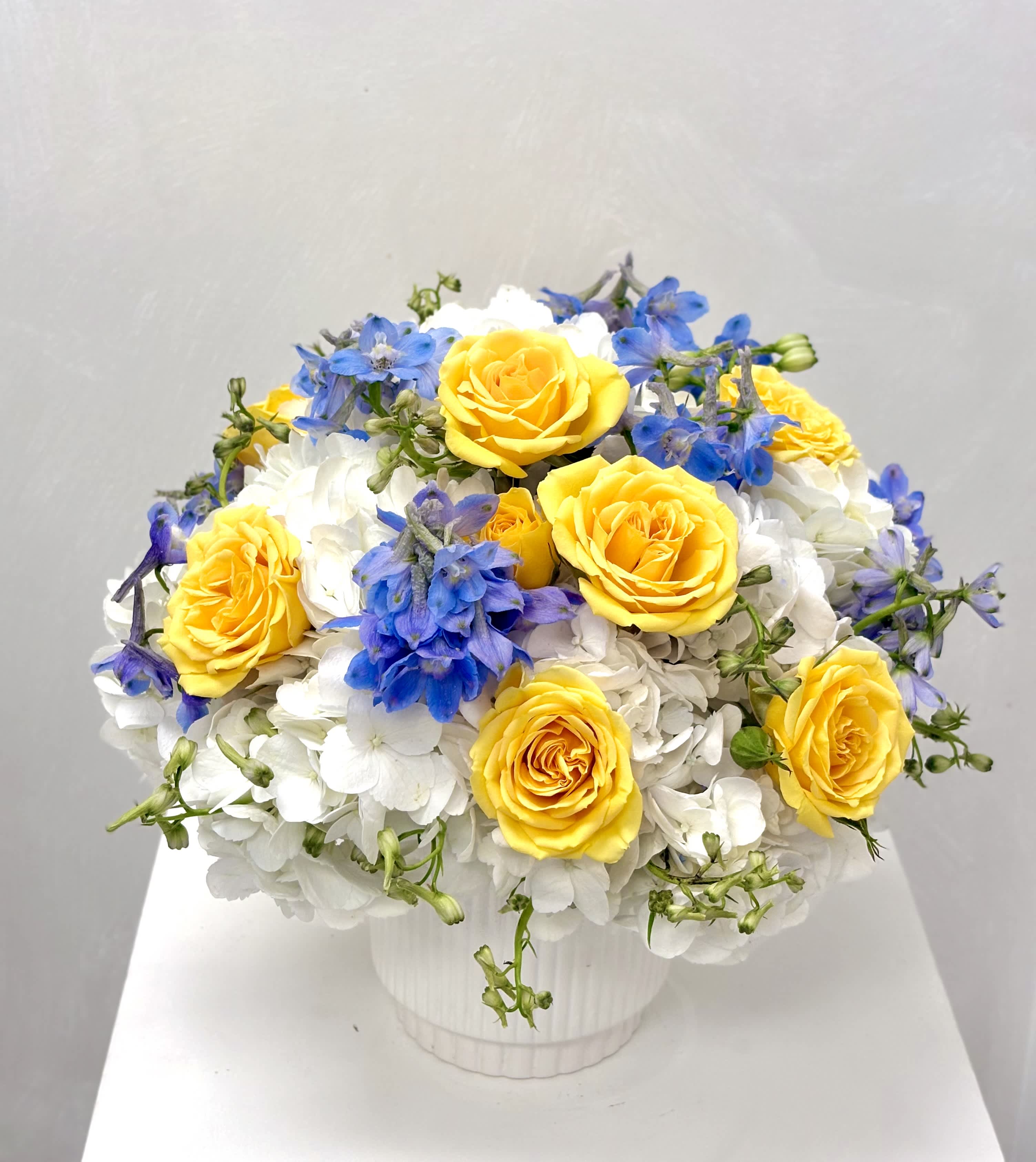 Yellow roses and blue flowers arranged in a white vase