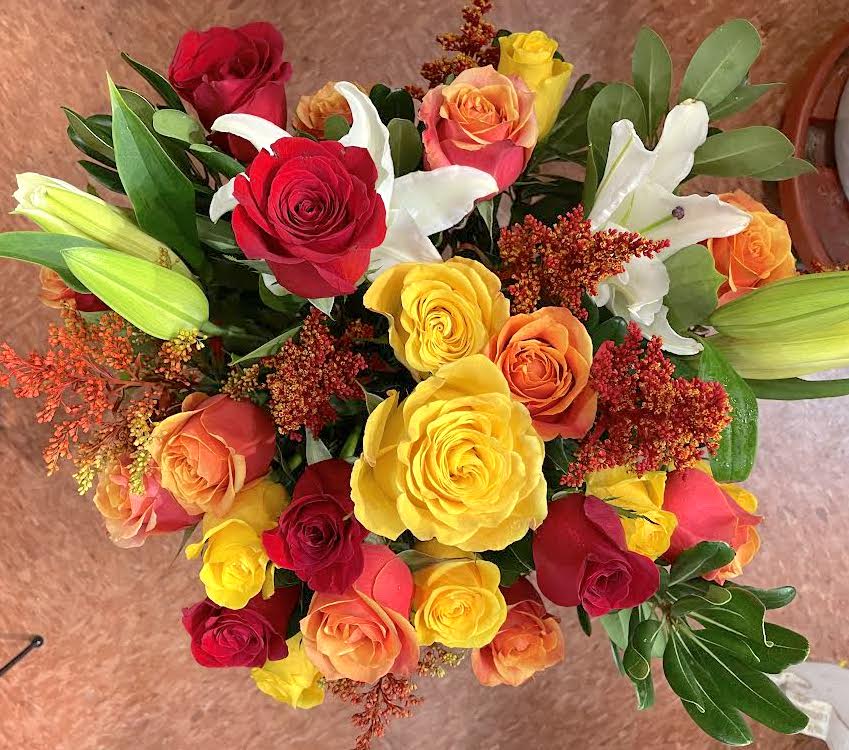 Top view of bright bouquet of red, yellow, and orange roses with white lilies