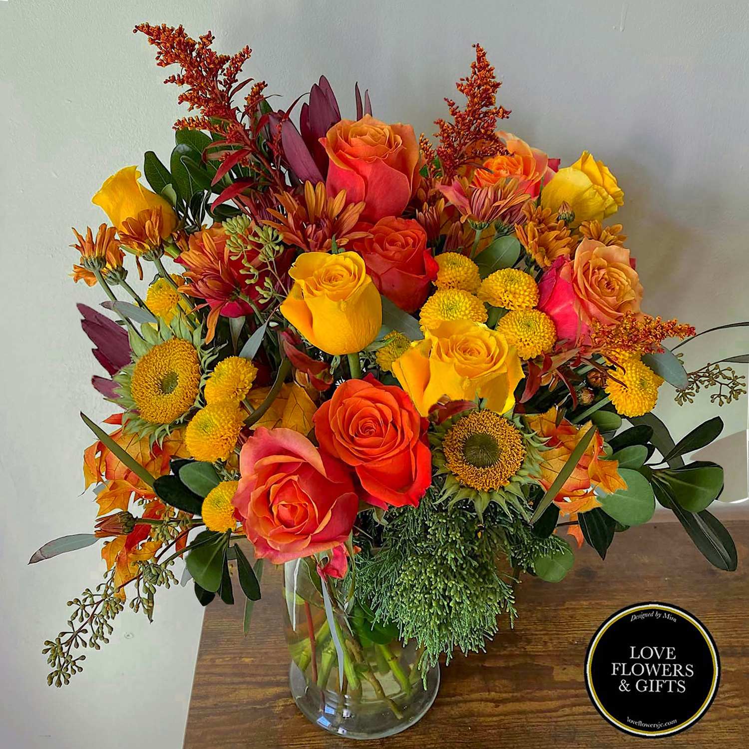 Vibrant arrangement of orange and yellow roses with yellow mums in a clear glass vase