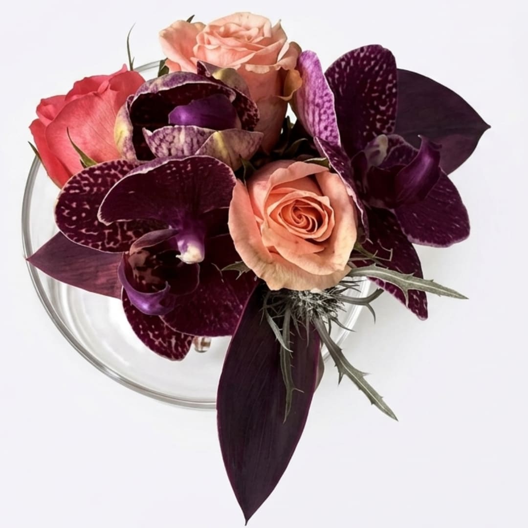 Compact bouquet of peach roses and purple orchids in a clear vase