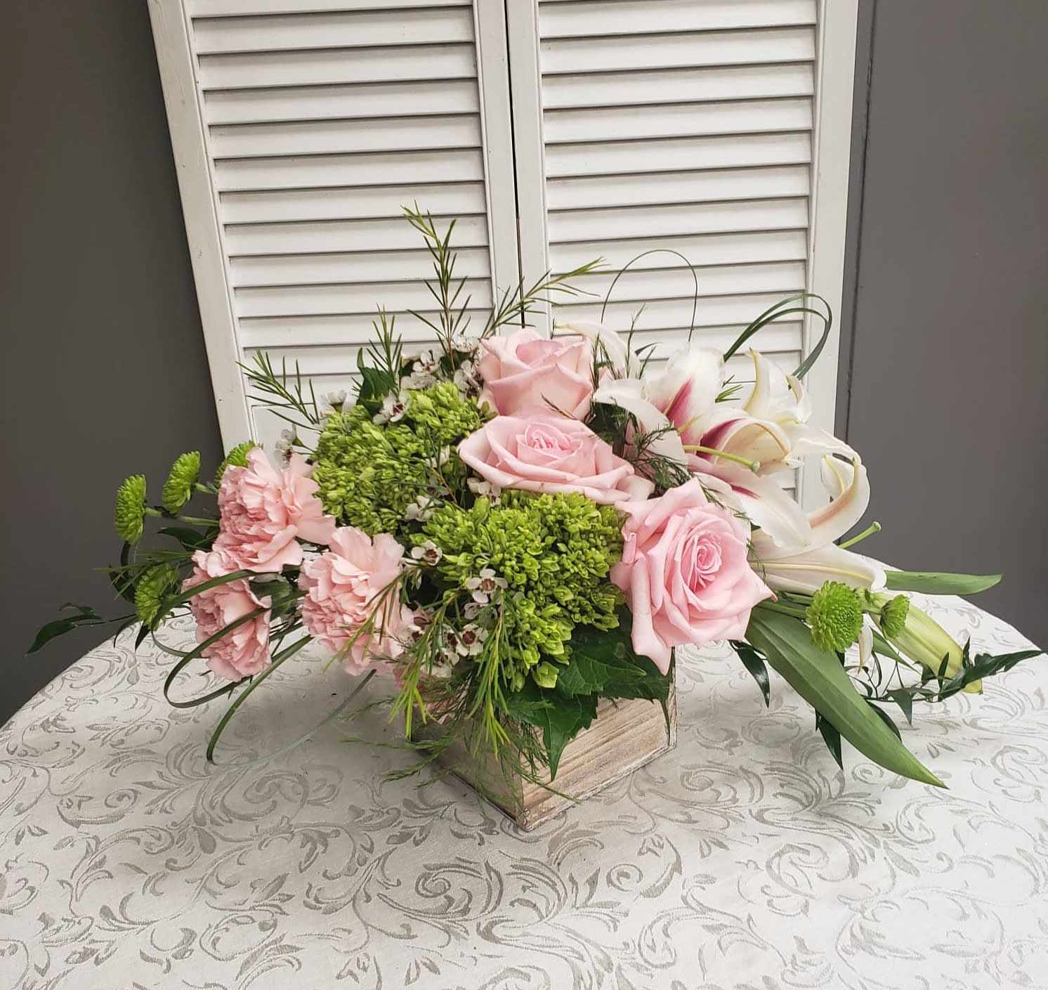Low centerpiece of pink roses, pink carnations, green hydrangea and white lilies in a wooden cube vase
