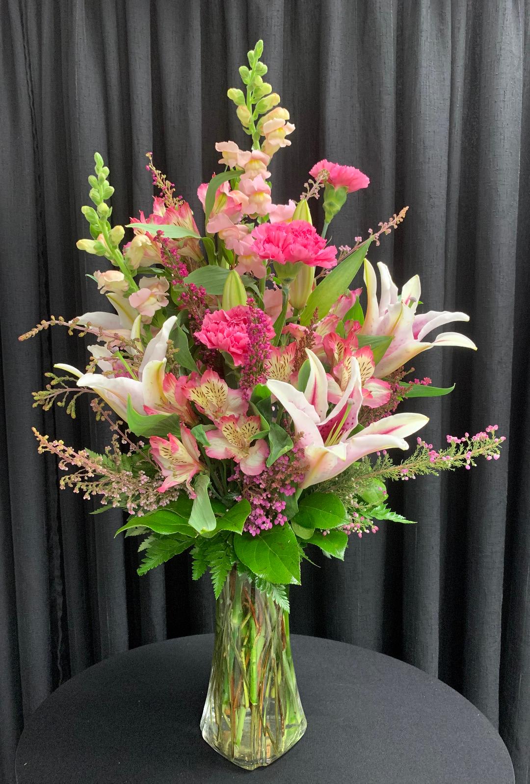 Tall pink and white lily and carnation arrangement with snapdragons in a clear glass vase