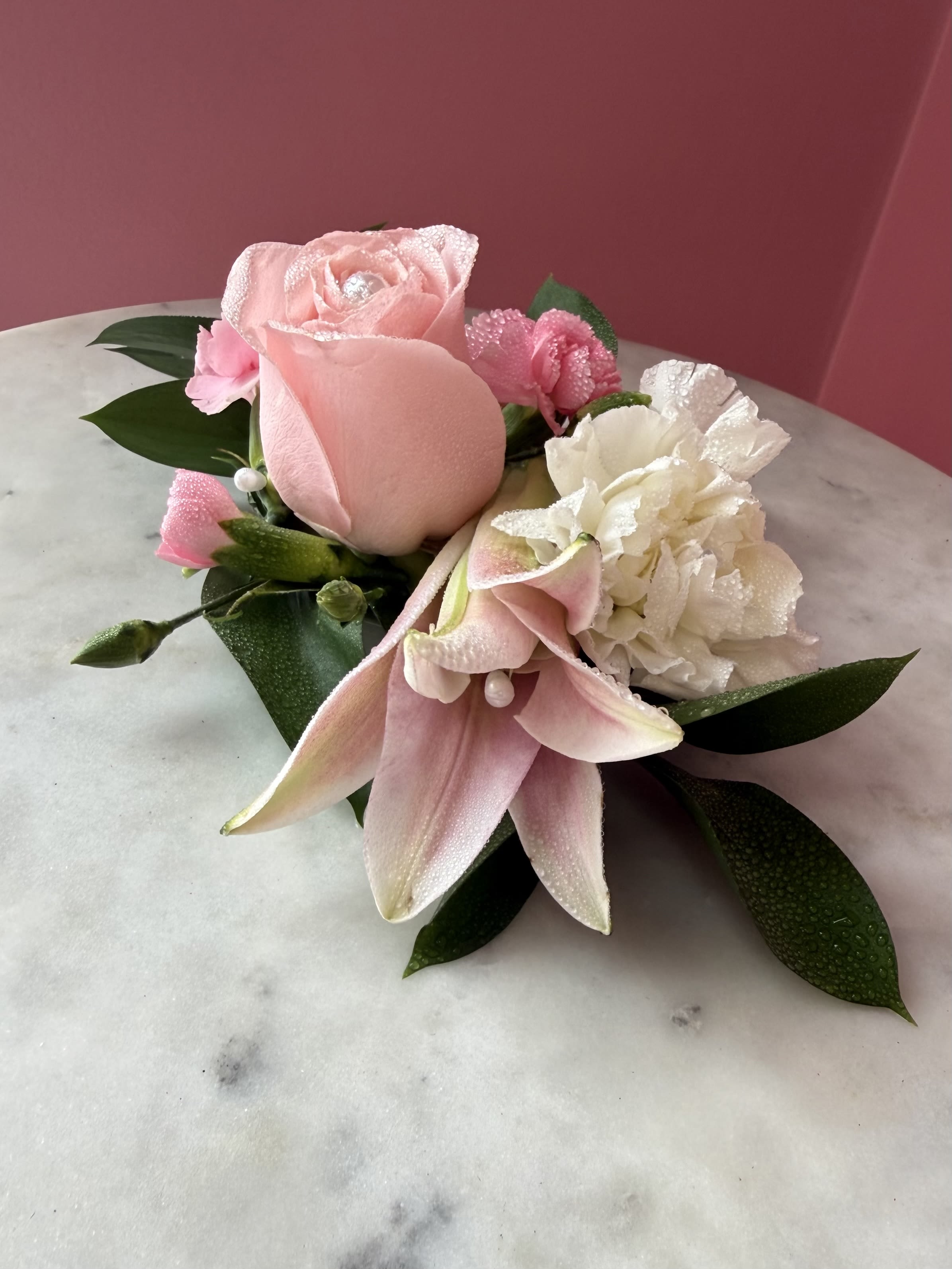 Premier Lily &amp; Pearls Corsage by Evergreen Elegance  - Pink Lily : The elongated, unopened bloom is a pink Oriental or Asiatic lily bud, which adds a graceful, tapering line to the design.  This design is a modern take on the traditional wristlet, making it a popular choice for proms, weddings, or formal galas. 