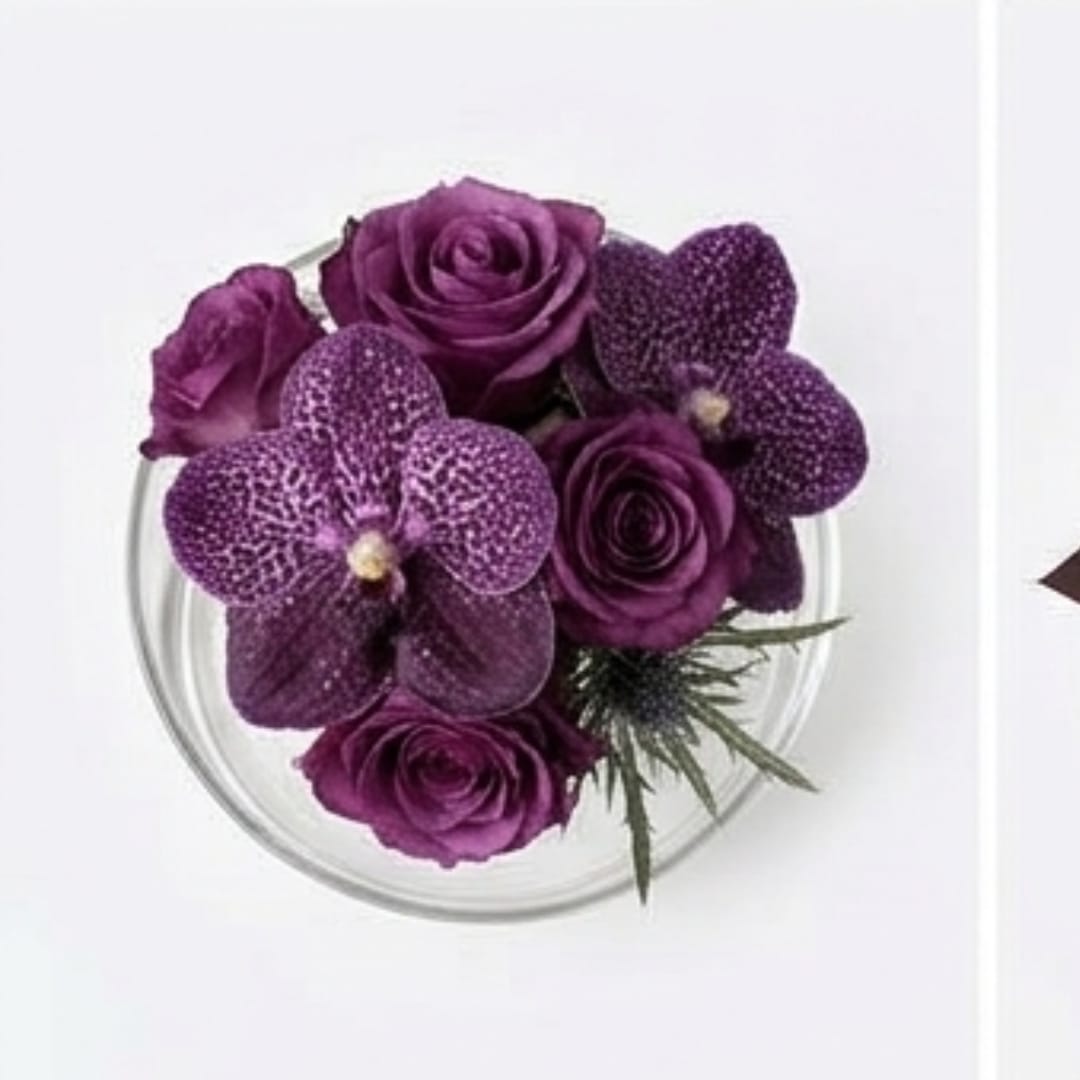 Purple roses and orchids arranged in a clear round vase