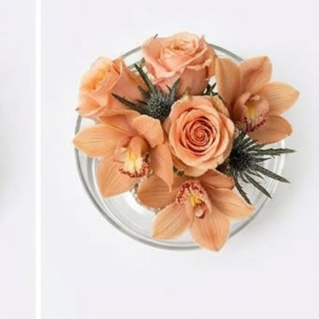 Peach roses and orchids arranged in a clear round vase