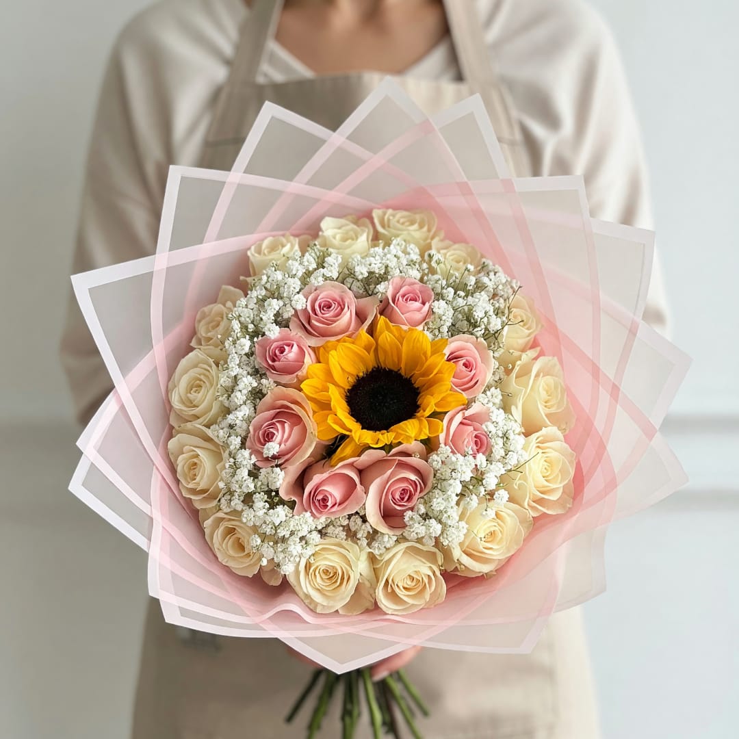 Handheld bouquet of pink and cream roses with a sunflower center