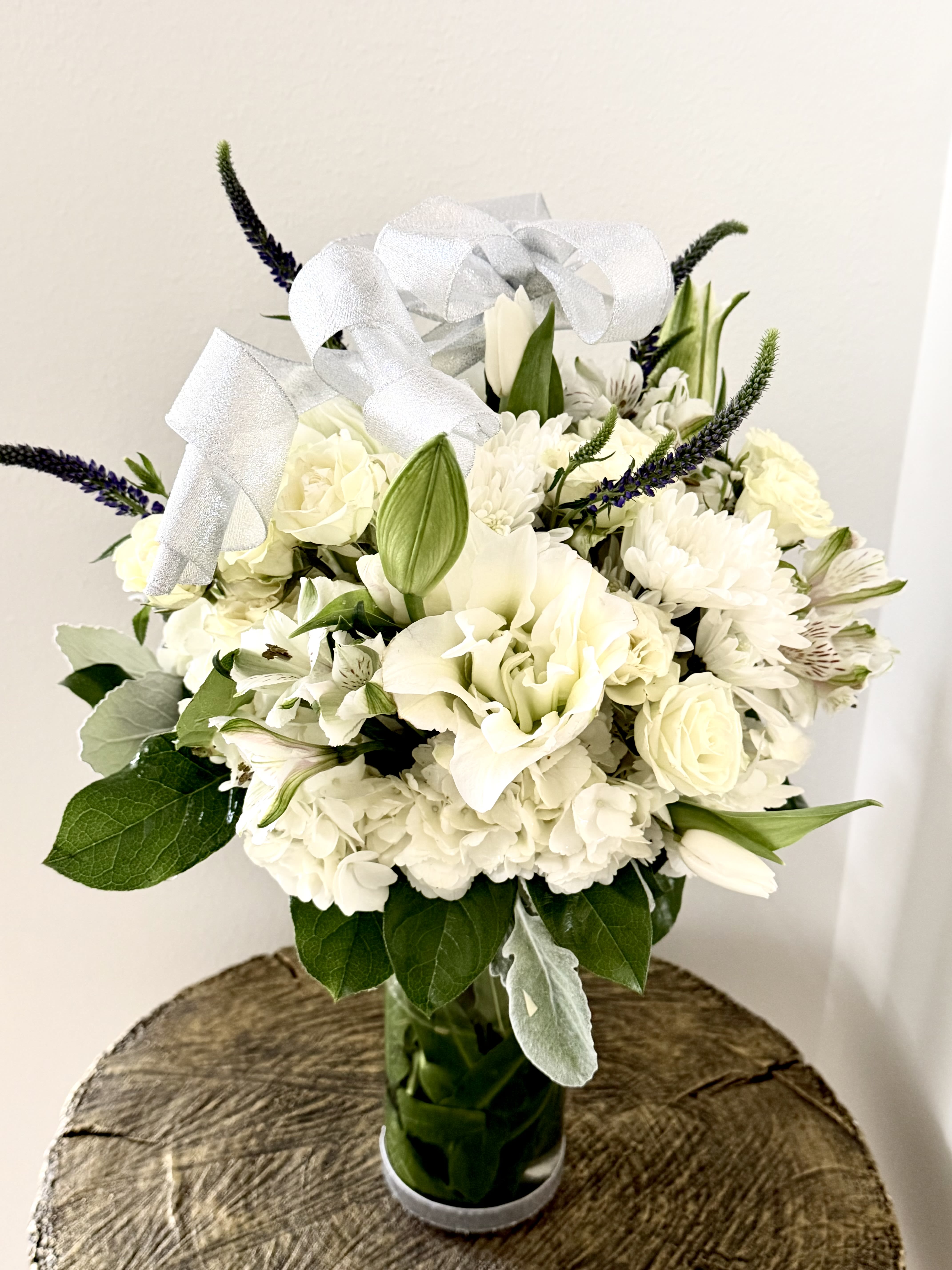 Silent Light - A white sympathy arrangement in a vase offers a timeless expression of peace, remembrance, and heartfelt condolences.Soft white blooms of hydrangeas,  lilies, roses, and chrysanthemums create a graceful tribute that honors a loved one with purity and dignity.