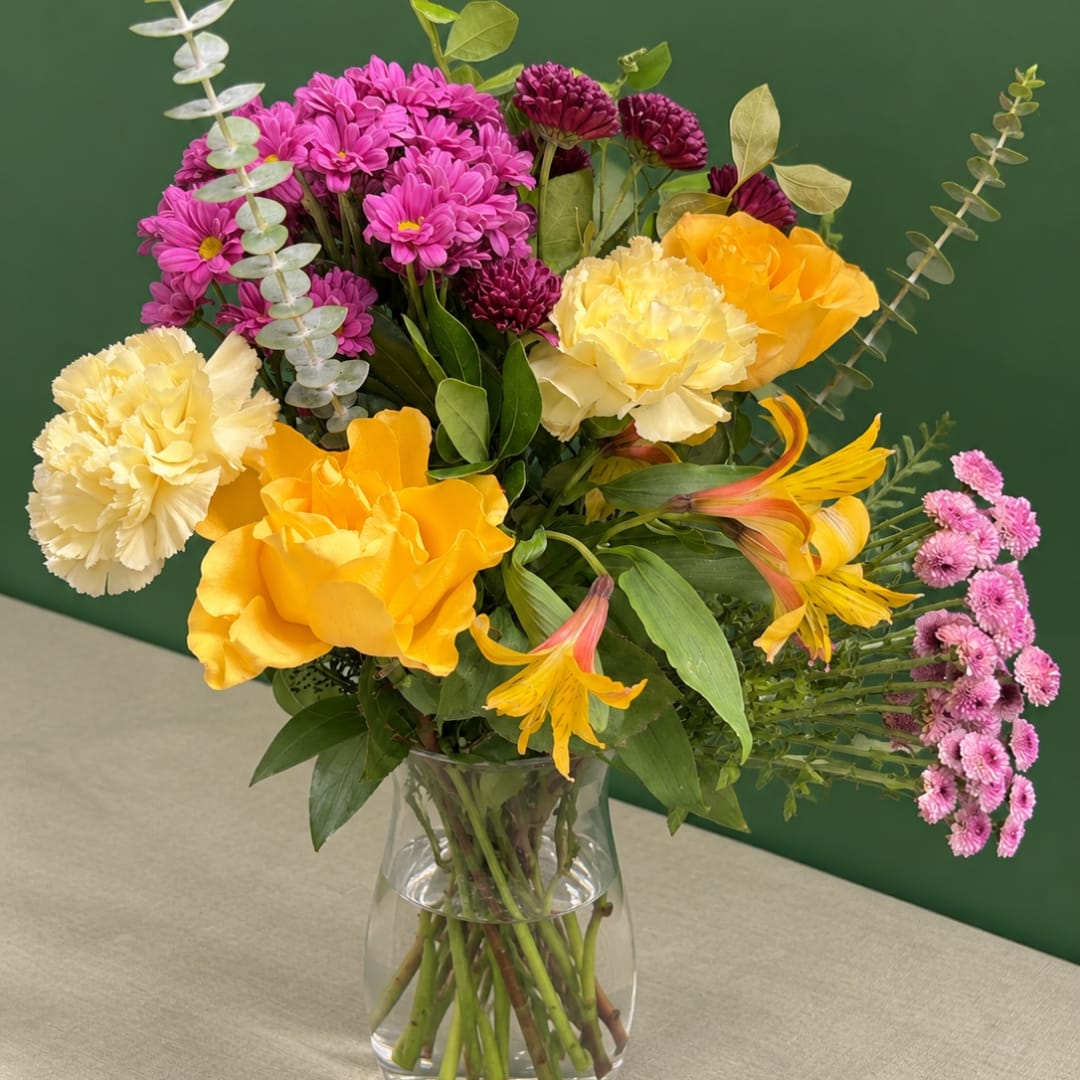 Mixed bouquet of yellow, pink, and purple flowers in a clear glass vase