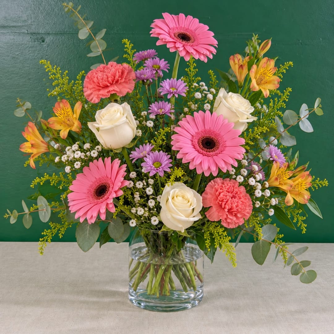 Pink gerbera daisies, white roses, and mixed blooms in a clear glass vase