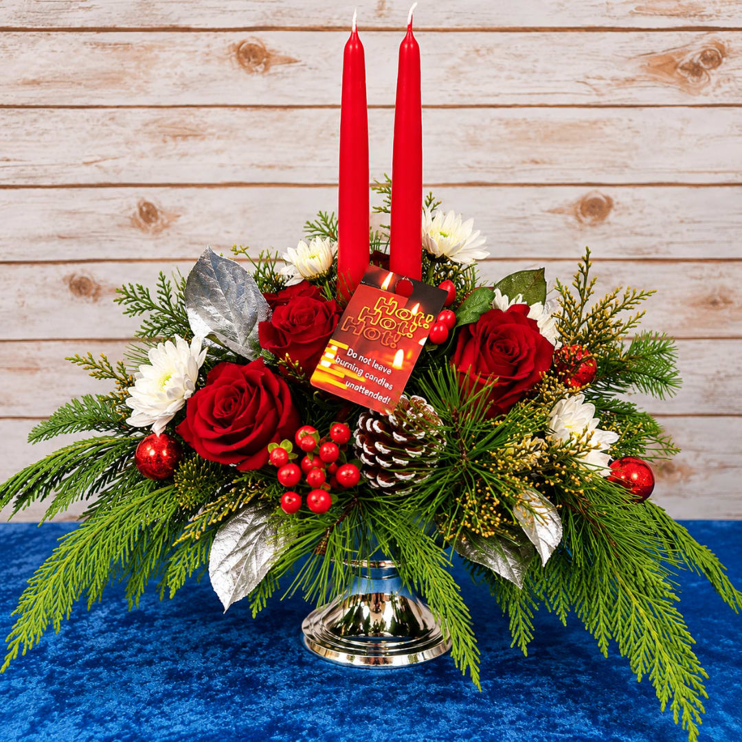 Holiday centerpiece with red candles, roses, and white daisies in a silver vase