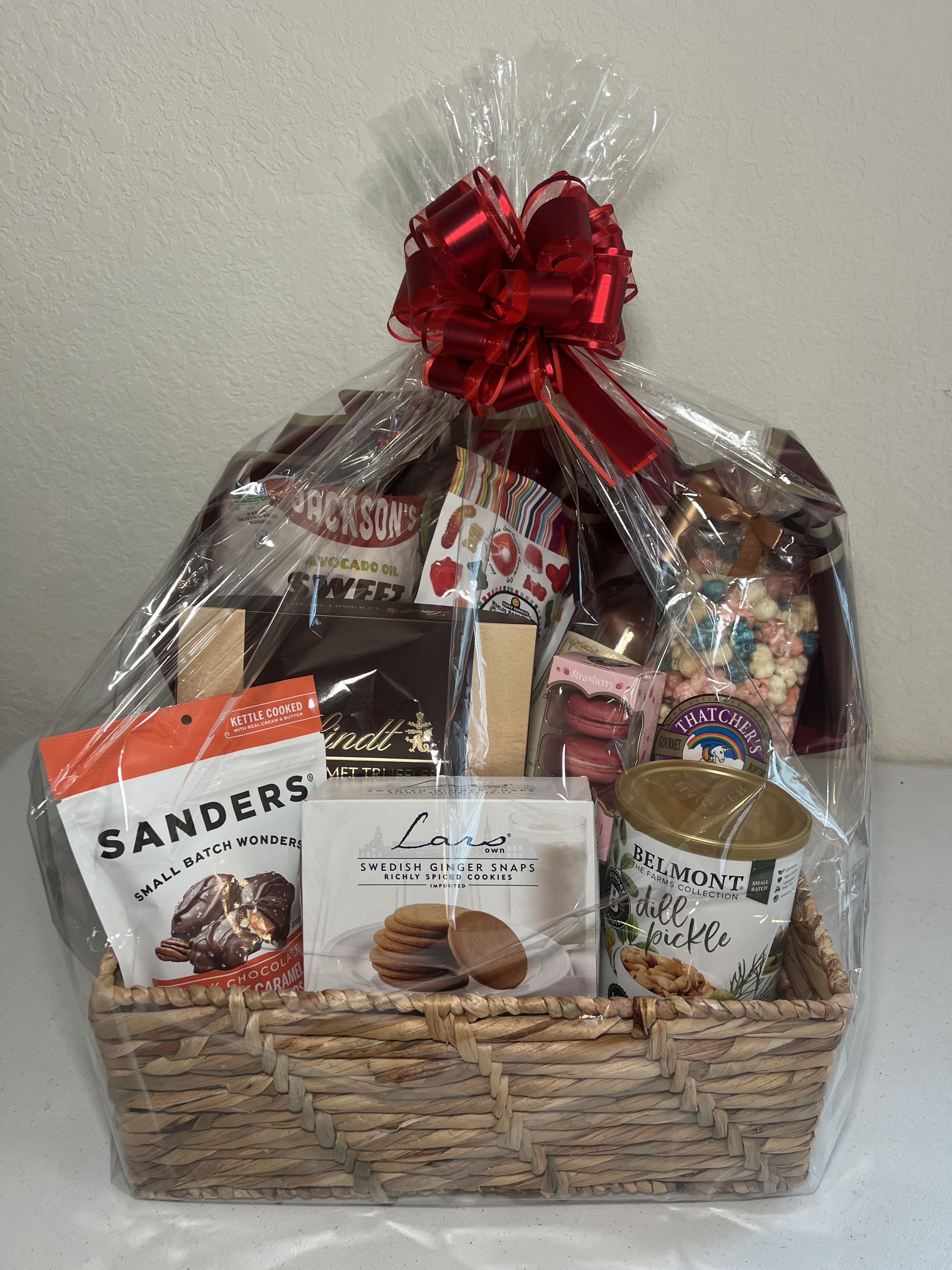 Gift basket of assorted snacks and sweets wrapped in clear cellophane with a red bow