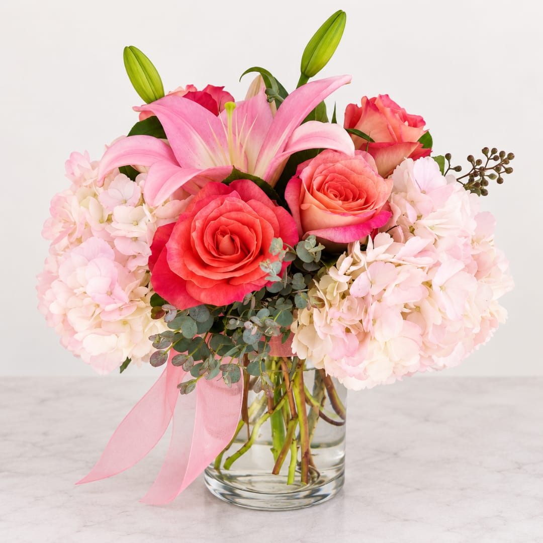 Pink lilies and roses in a clear glass vase with hydrangeas