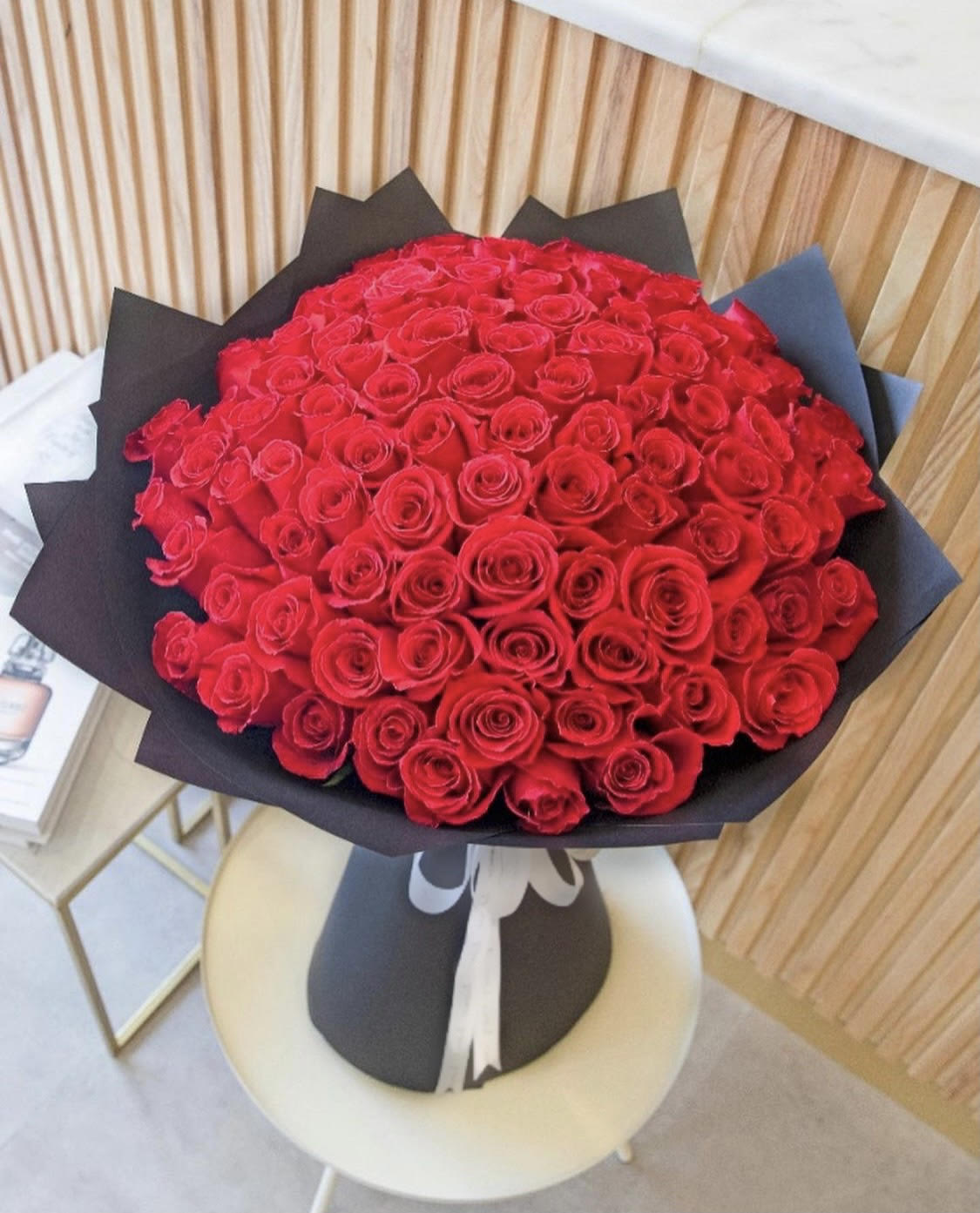 Large bouquet of tightly clustered red roses wrapped in black paper and tied with a white ribbon