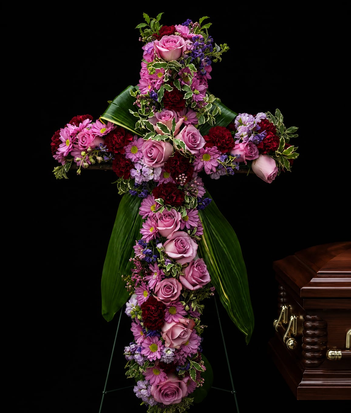 Royal Farewell  - A graceful floral cross designed to honor a life of faith, love, and cherished memories. Featuring a beautiful blend of soft pinks, rich tones, and lush greenery, this tribute offers comfort, peace, and a heartfelt expression of remembrance. 