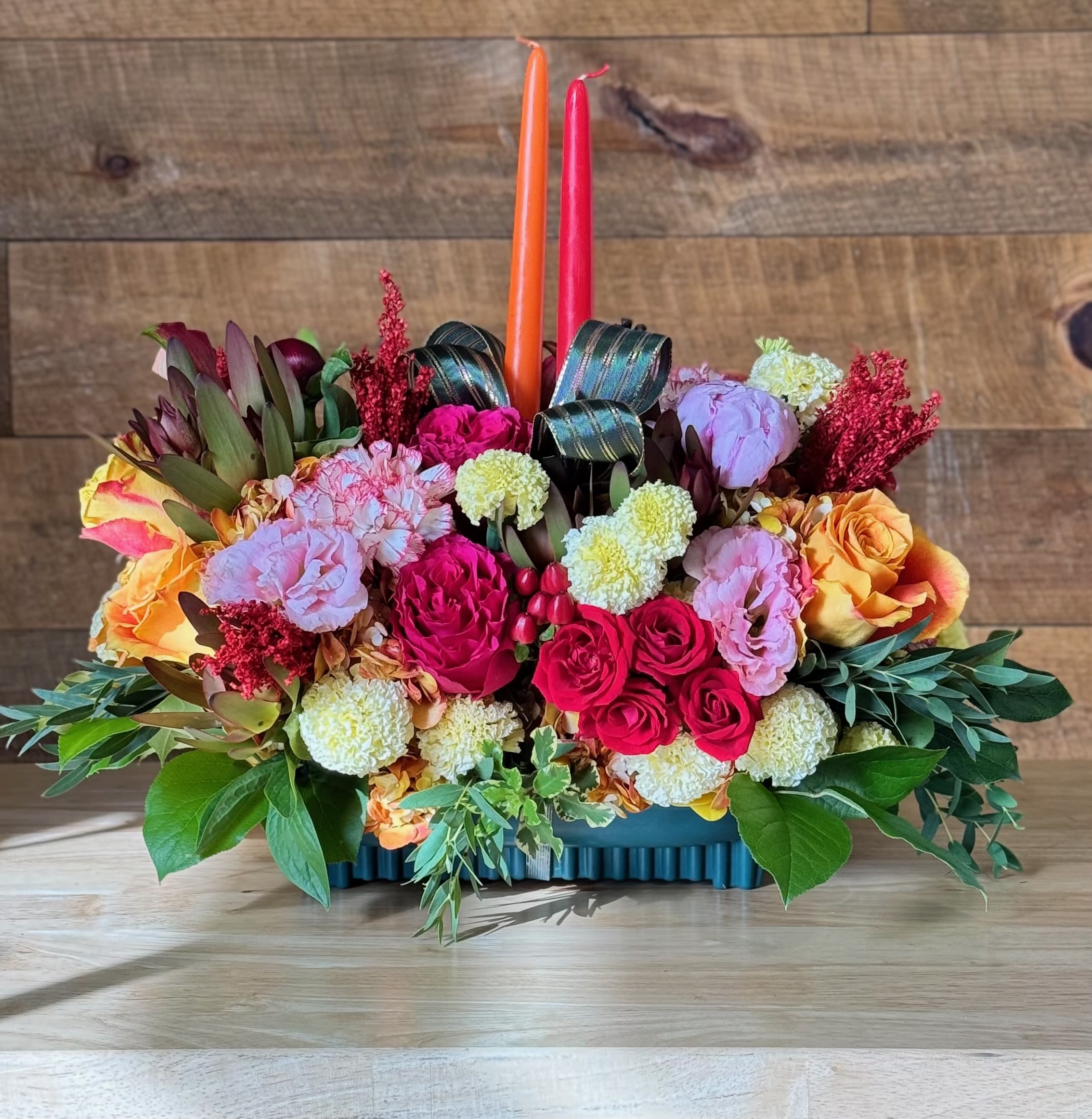 Colorful floral centerpiece with two taper candles in a low rectangular container