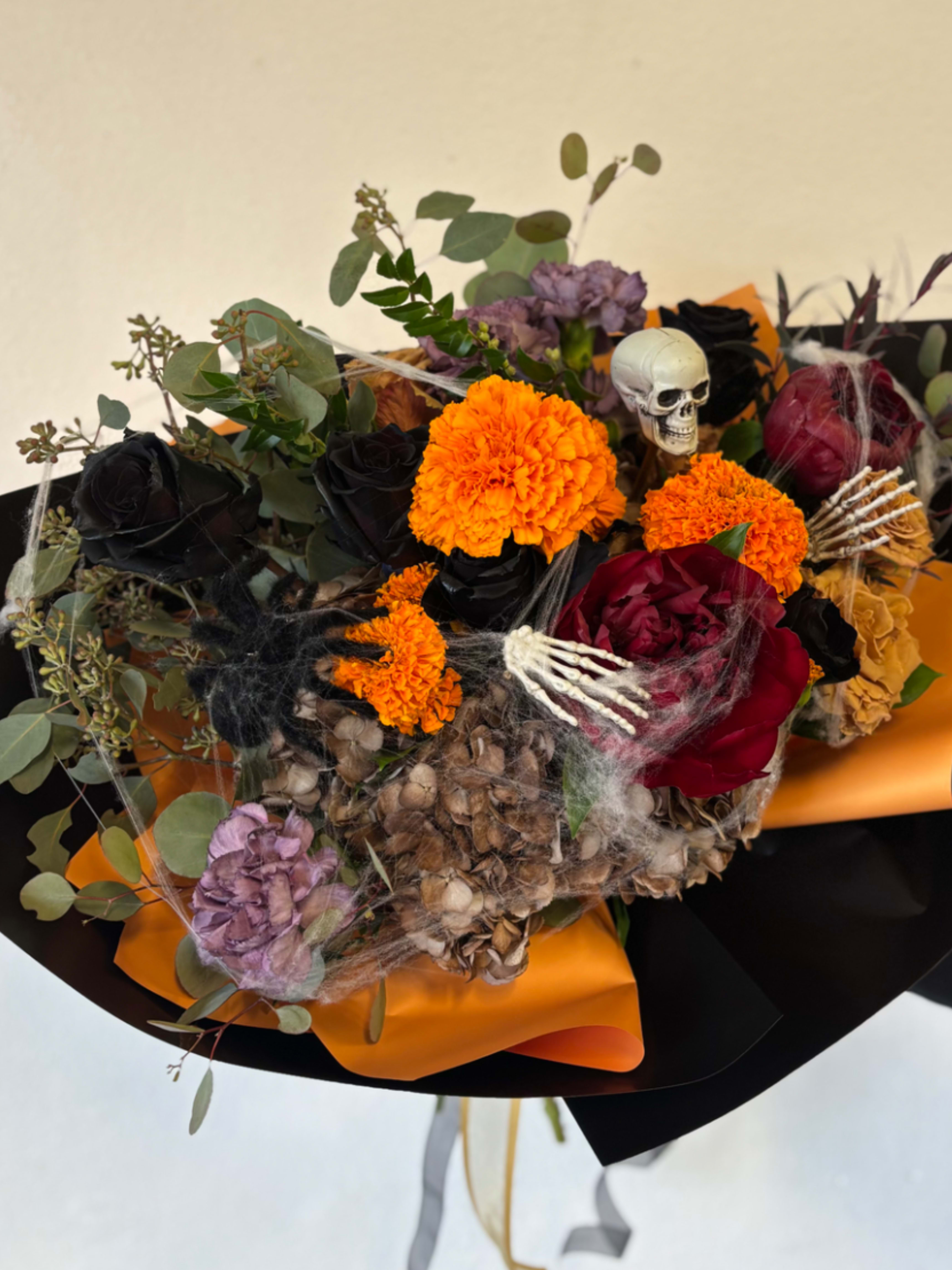Halloween bouquet with orange marigolds, dark roses, and a small skull accent
