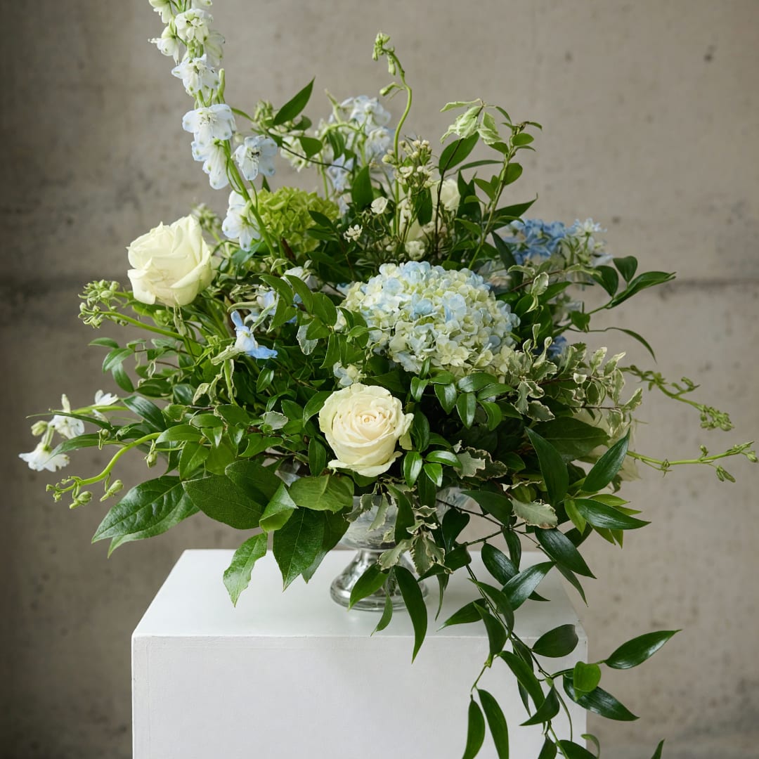 White roses and blue hydrangea in a glass vase with trailing greenery