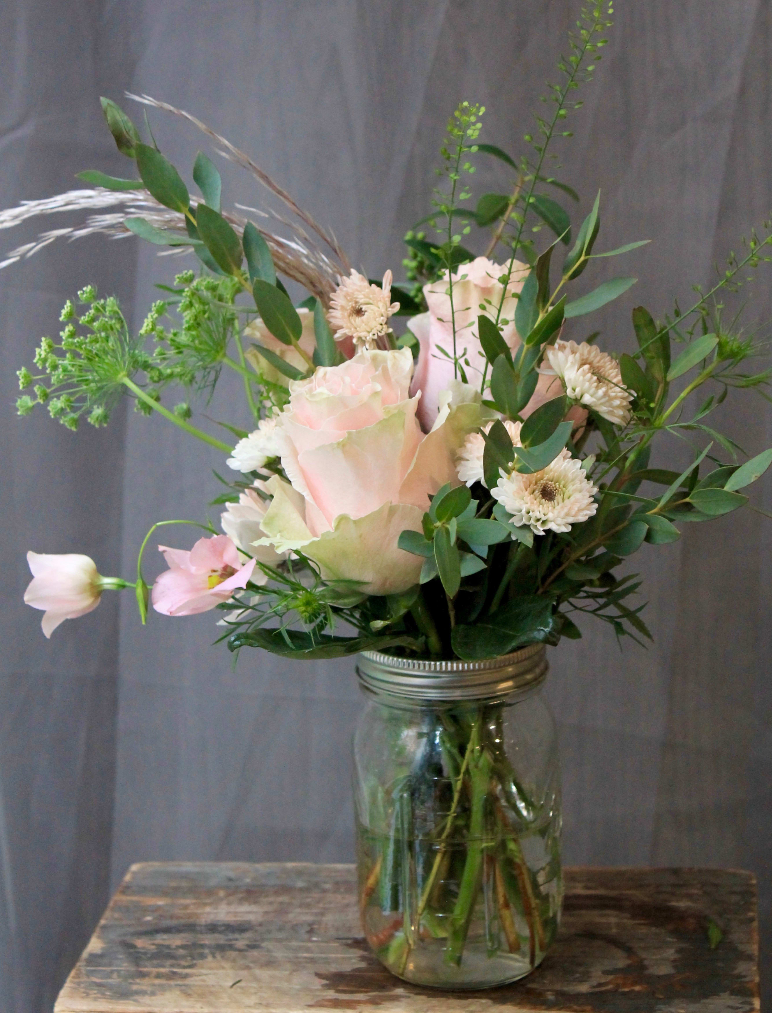 Pink roses and white daisies arranged in a glass jar vase
