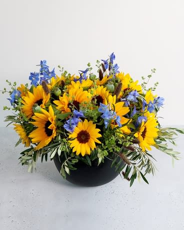 Yellow sunflowers and blue flowers in a black bowl vase