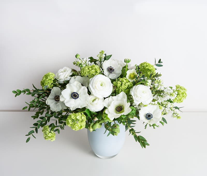 White flowers and green blooms arranged in a pale blue vase