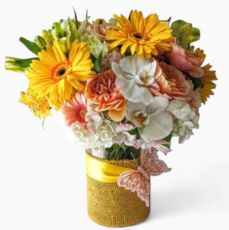 Vase arrangement of yellow gerbera daisies, peach roses, and white orchids in a yellow-wrapped cylinder vase