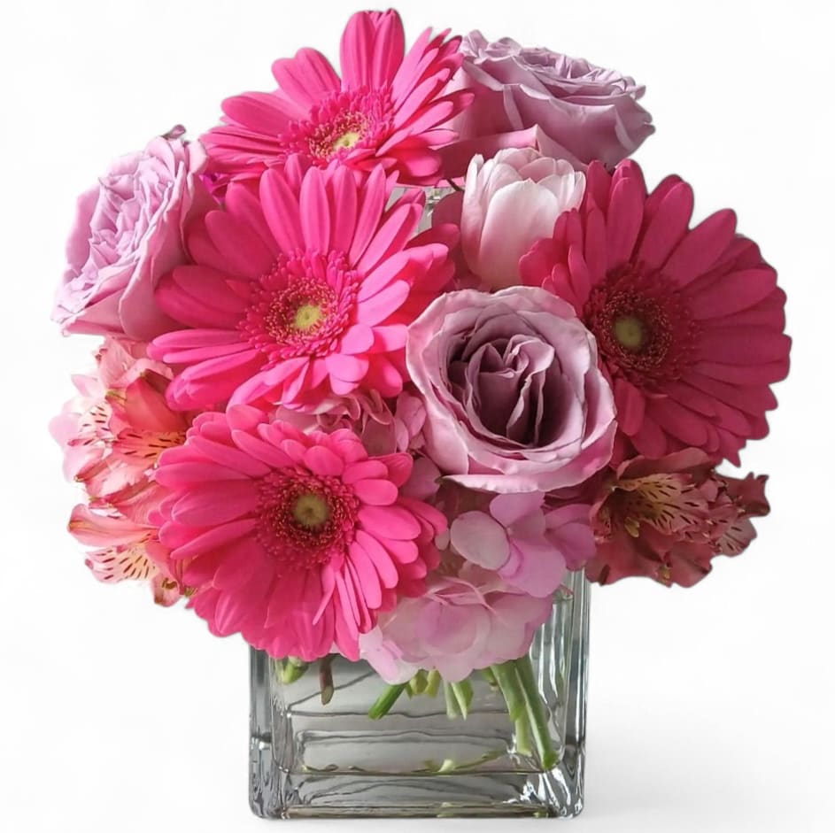 Pink gerbera daisies and roses arranged in a clear square vase