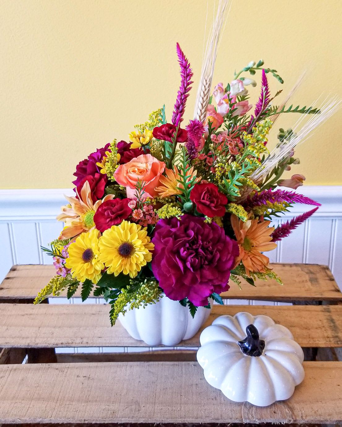Colorful flower arrangement in a white pumpkin-shaped vase with a small white pumpkin decor piece nearby.