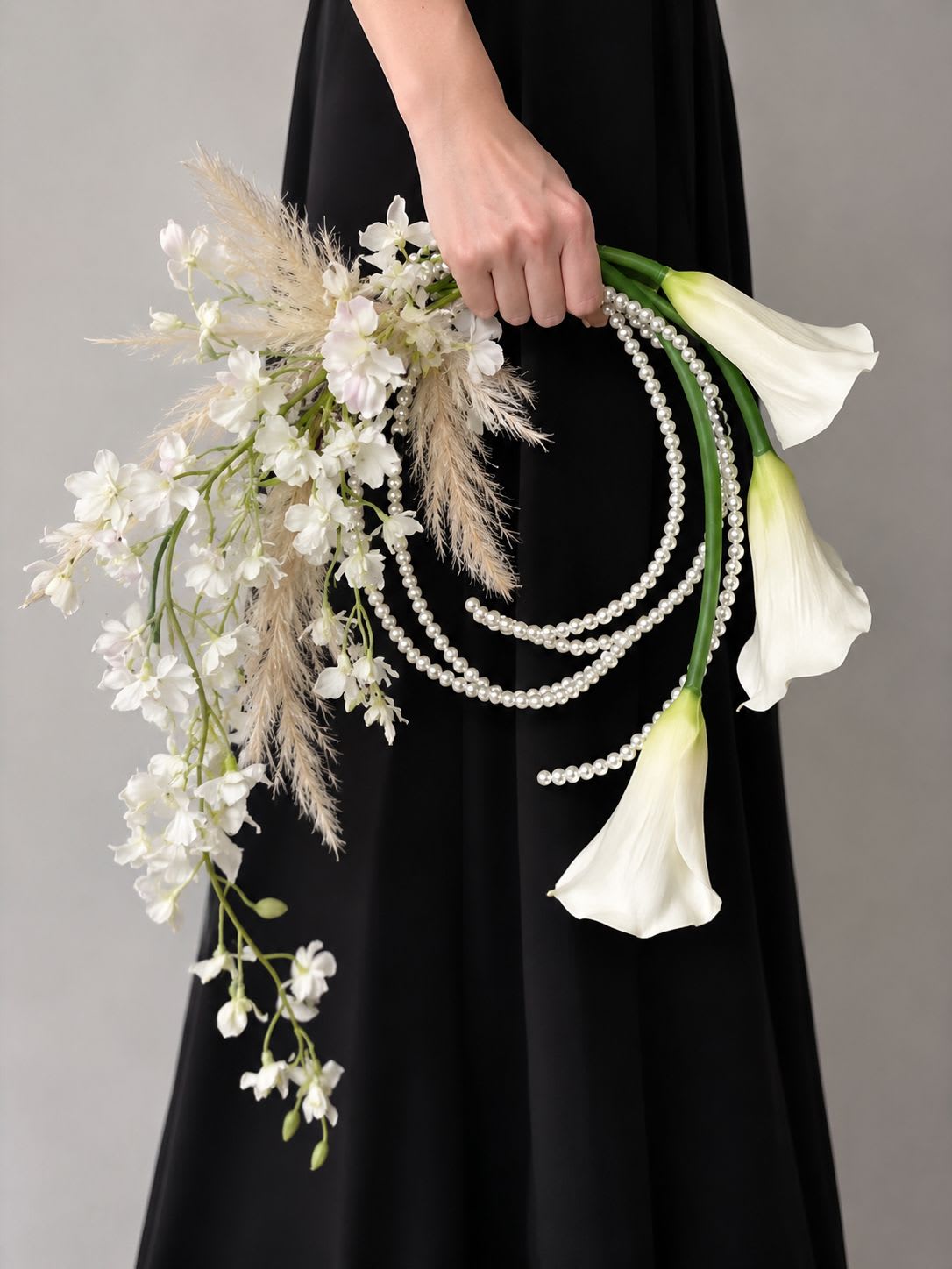 Calla lily  &amp; Pampas Pearl Bridal Bouquet - A refined bridal bouquet designed for the modern bride who loves timeless elegance with an artistic touch. This contemporary design features graceful white calla lilies paired with soft ivory pampas grass and delicate cascading white blooms, creating a light, airy silhouette. Flowing pearl strands add a luxurious couture-inspired finish, making this bouquet a true statement piece for weddings, editorial shoots, and upscale ceremonies. Includes: Premium white calla lilies Ivory pampas grass Delicate cascading white accent flowers Elegant pearl detailing Handcrafted designer finish